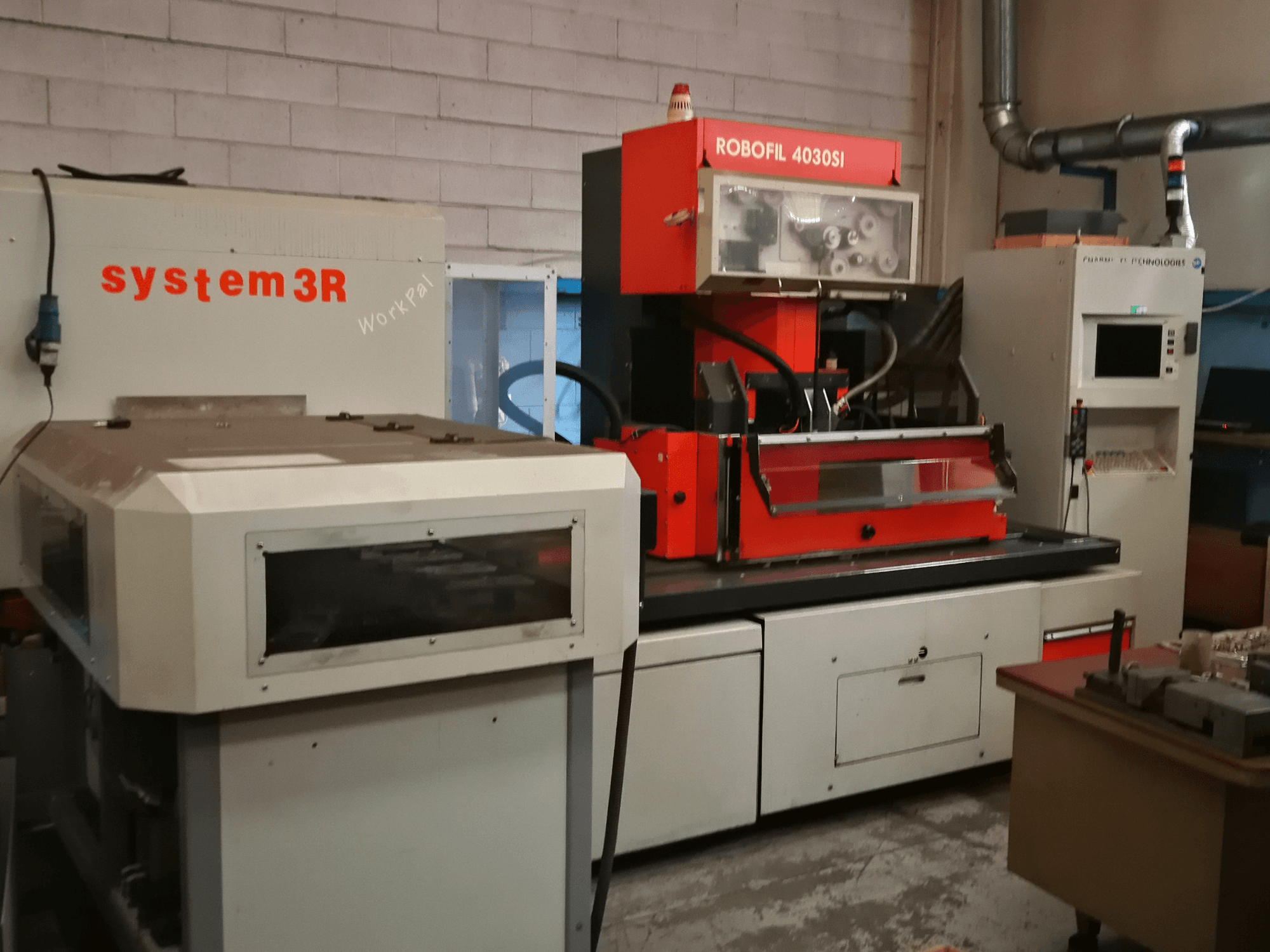 Frontvy av CHARMILLES ROBOFIL 4030 Si trådgnistmaskin, med röd och grå exteriör och intilliggande system3R-arbetsstation.