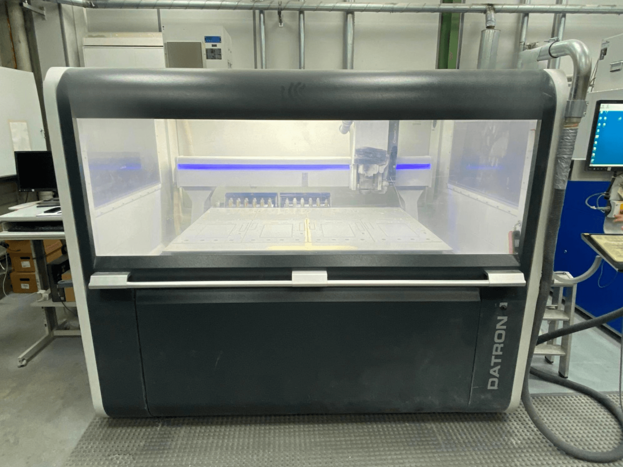 Frontvy av Datron MLCube B vertikalt bearbetningscenter, som visar det genomskinliga höljet och kontrollpanelen.