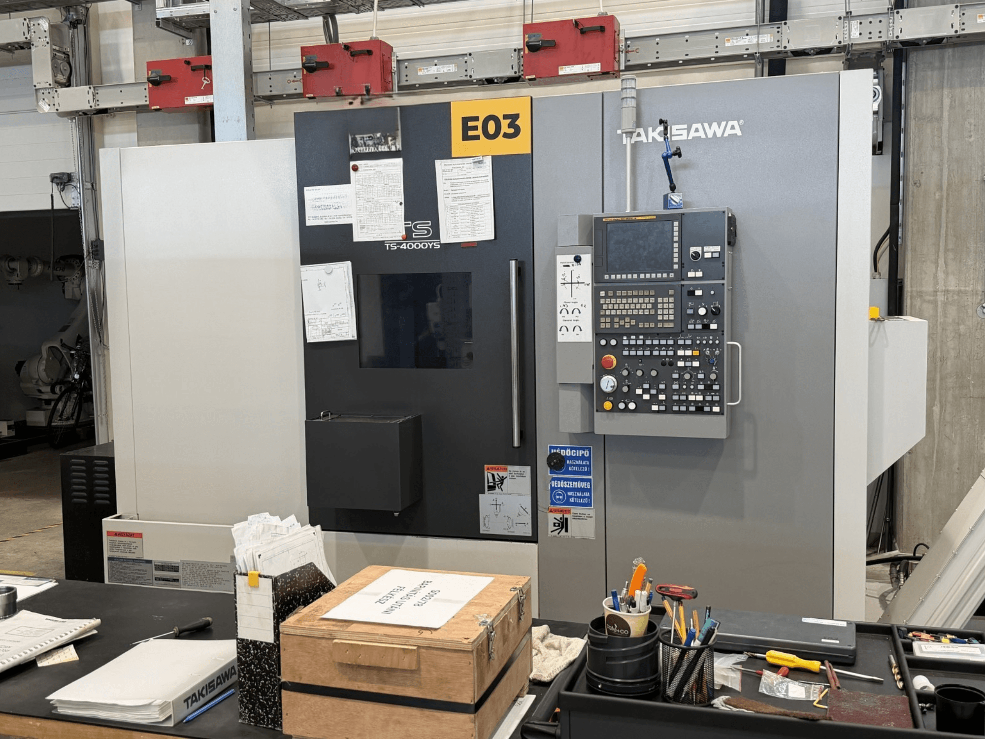 Takisawa TS-4000YS-svarv- och fräsmaskin sedd framifrån, med kontrollpanelen och dokumenten synliga på sidan.