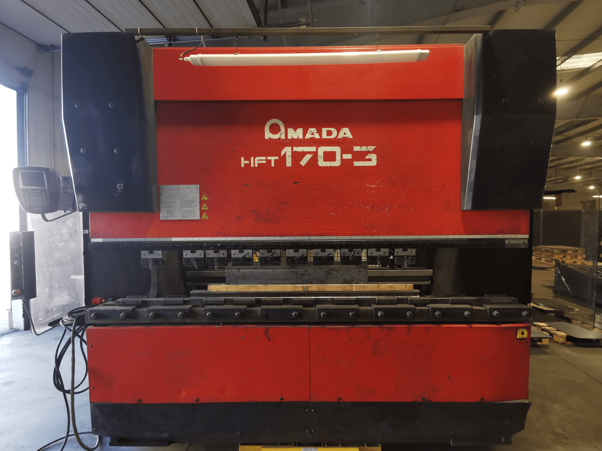 Röd Amada HFT 170-3 kantpress sedd framifrån, med kontrollpanel, bockverktyg och arbetsyta.