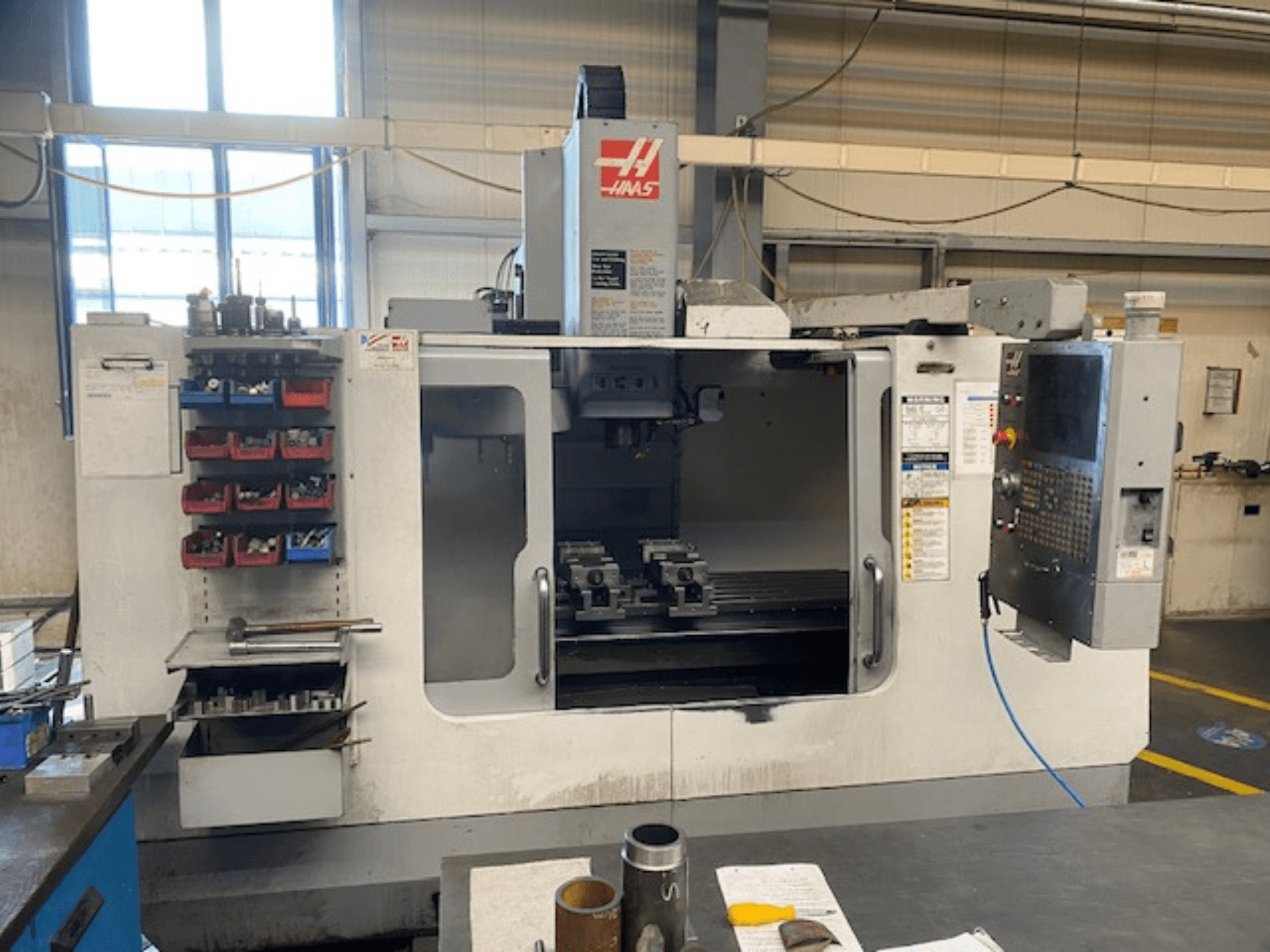 Haas CNC-fräsmaskin framifrån, modell VF-2, med verktygsförvaring, kontrollpanel och arbetsverktyg synliga.