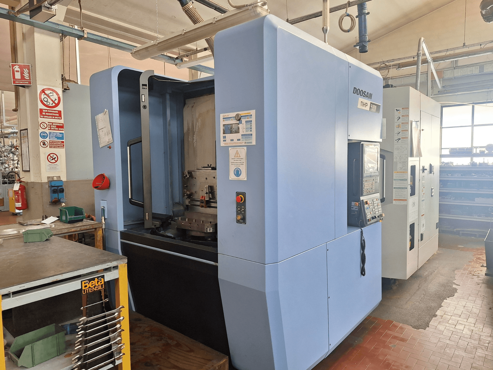 DOOSAN NHP 5000 horisontell fleroperationsmaskin i en verkstad, sidovy som visar kontrollpanelen och bearbetningsområdet.