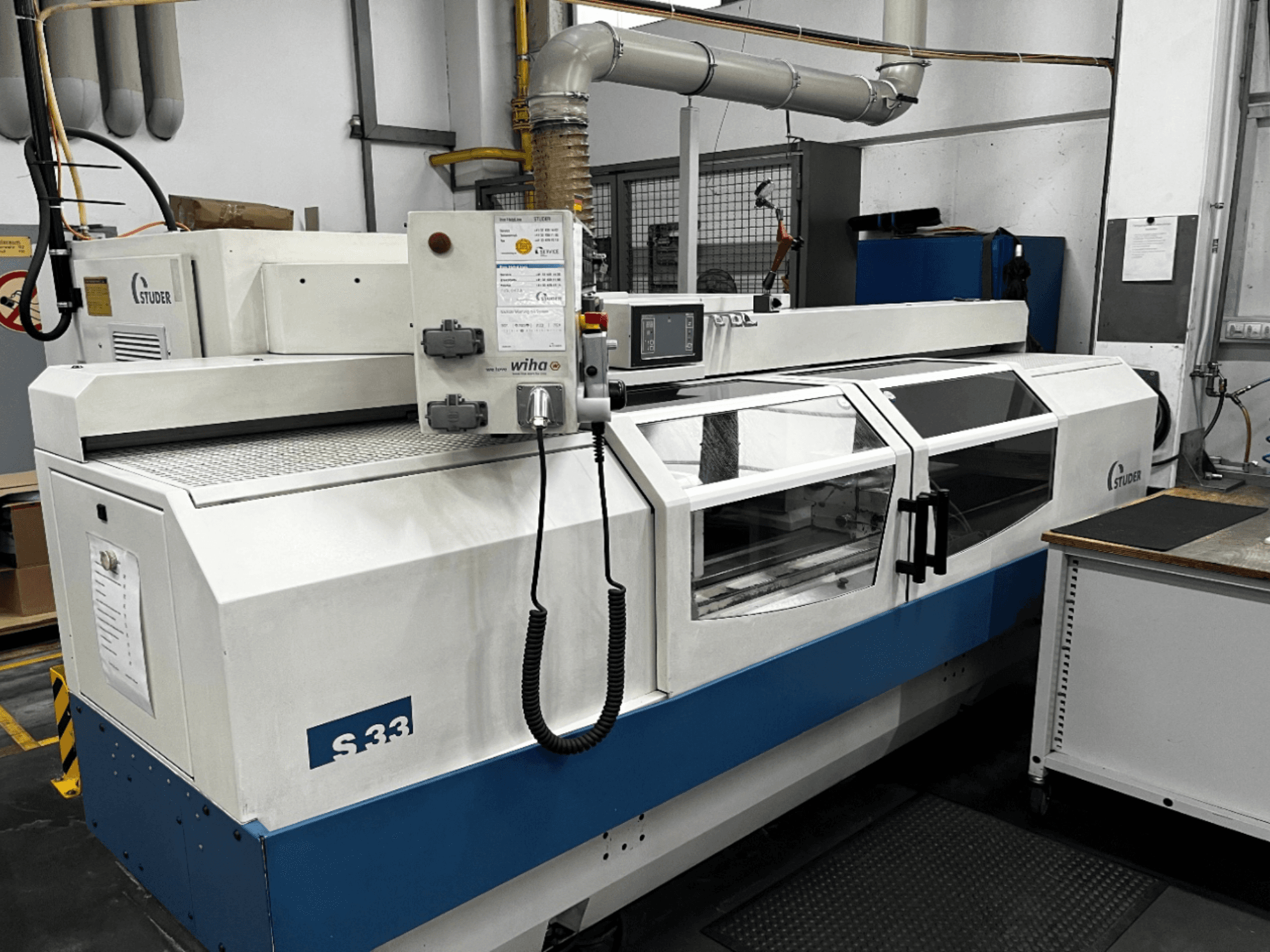 STUDER S33 CNC-cylindrisk slipmaskin, framifrån; har kontrollpanel och säkerhetsdörrar av glas. Industriell miljö.
