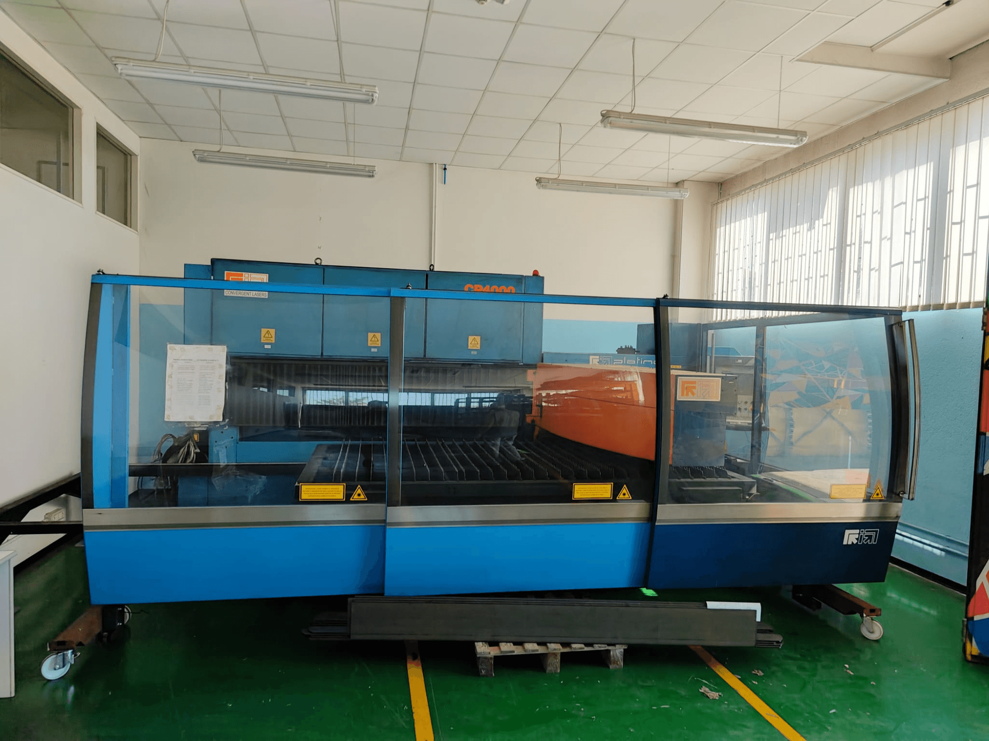 Framifrånbild av en CO₂-laserskärmaskin av modell CP4000 från CONVERGENT LASERS med blå och orange design, i en väl upplyst verkstadsmiljö.