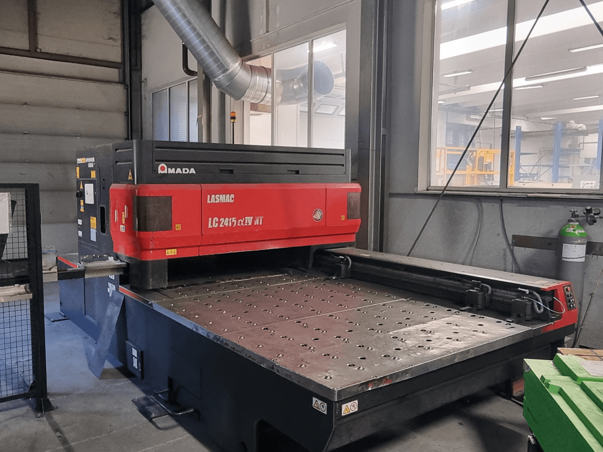 Amada LASMAC LC 2415 αⅡ NT laserskärmaskin i rött och svart, framifrån, med en driven skärbädd och precisionsreglage.