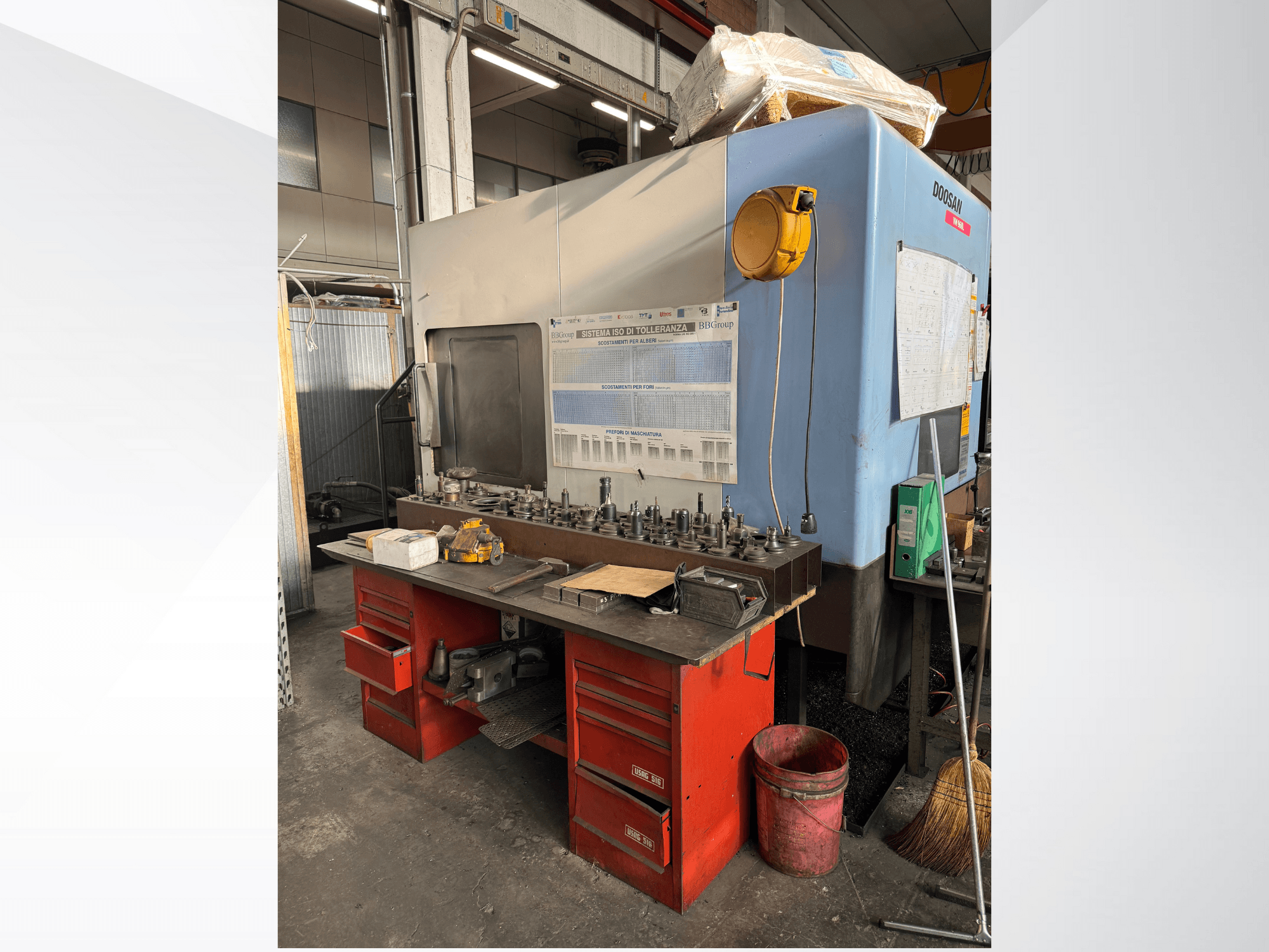 Doosan bearbetningscenter med röd arbetsbänk och förvaring, där verktyg och utrustning visas, sett framifrån.