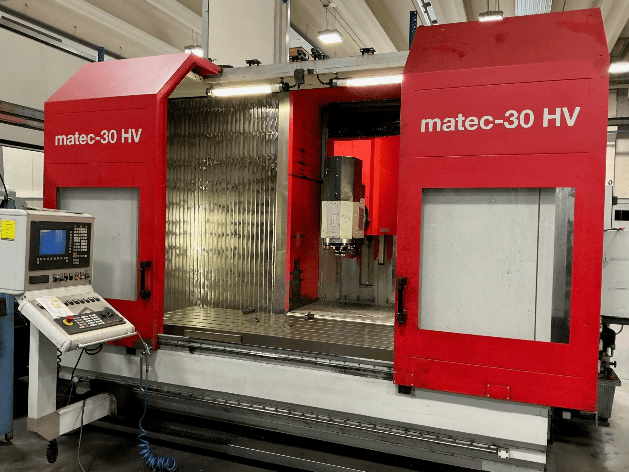 Red Matec 30 HV vertikal bearbetningscenter framifrån, med kontrollpanel och öppna dörrar som visar skärområdet.