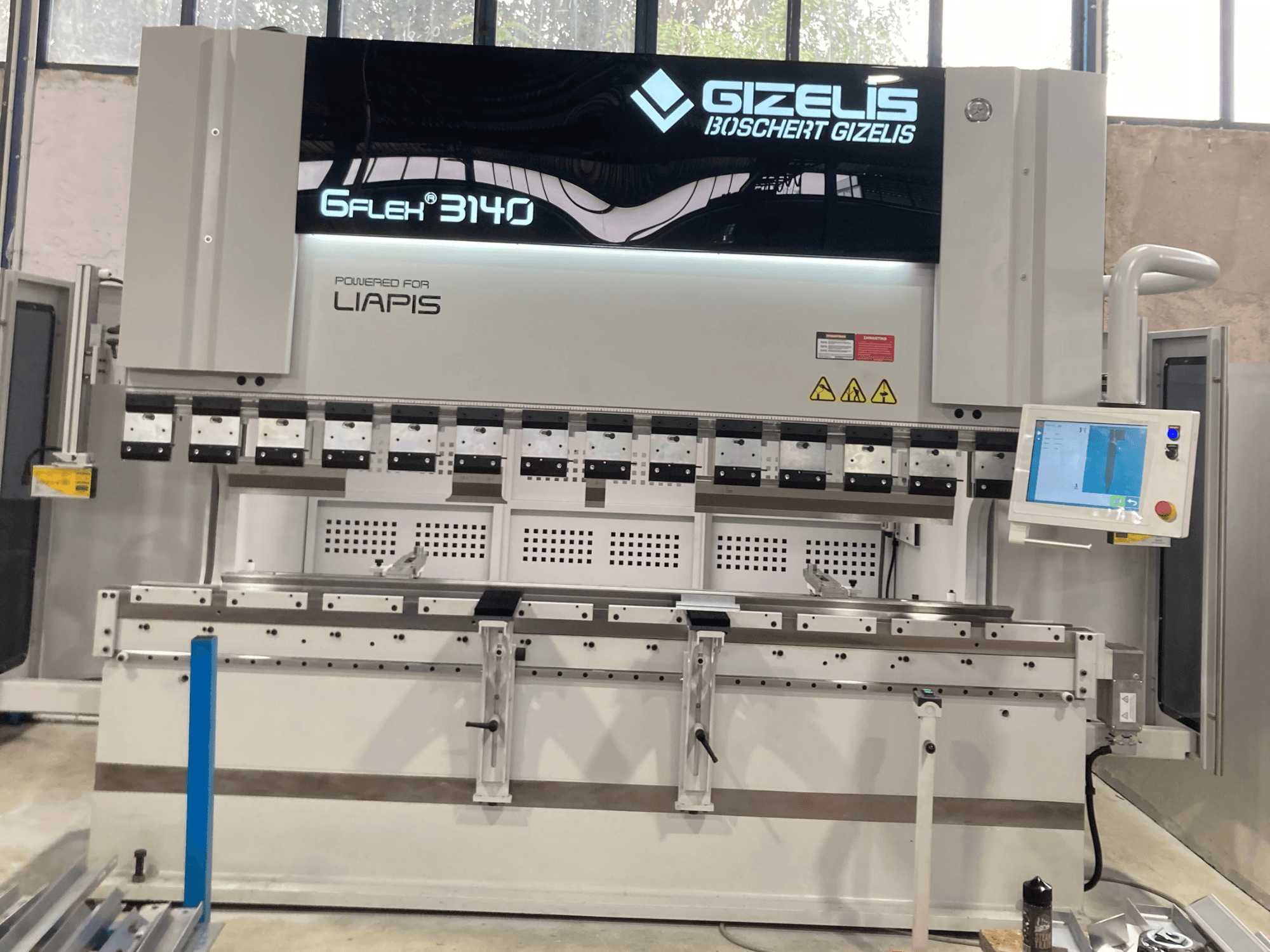 Hydraulisk press GIZELIS G-FLEX 3140 framifrån med kontrollskärm, med flera bockningsverktyg och säkerhetsetiketter.