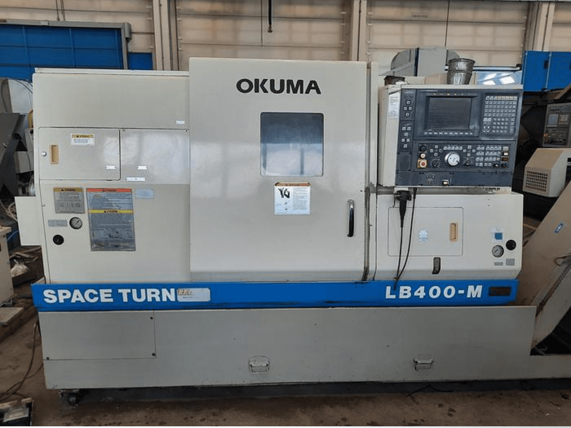 Okuma LB400-M CNC-svarv, framifrån med kontrollpanel, varningsetiketter och blå "SPACE TURN"-märkning synliga.