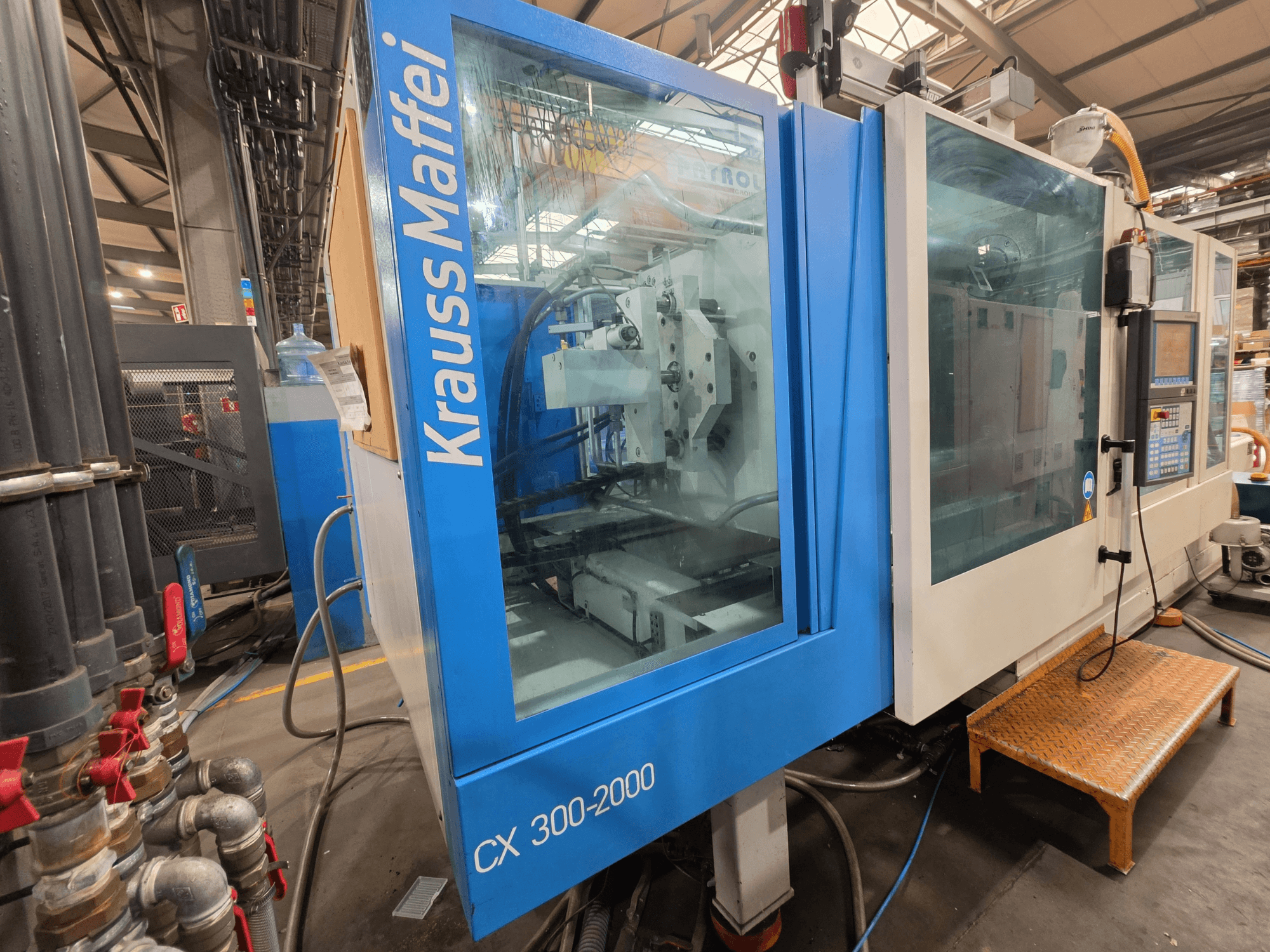 Krauss Maffei CX 300-2000 hydraulisk formsprutningsmaskin, framifrån med kontrollpanel och hydraulledningar.