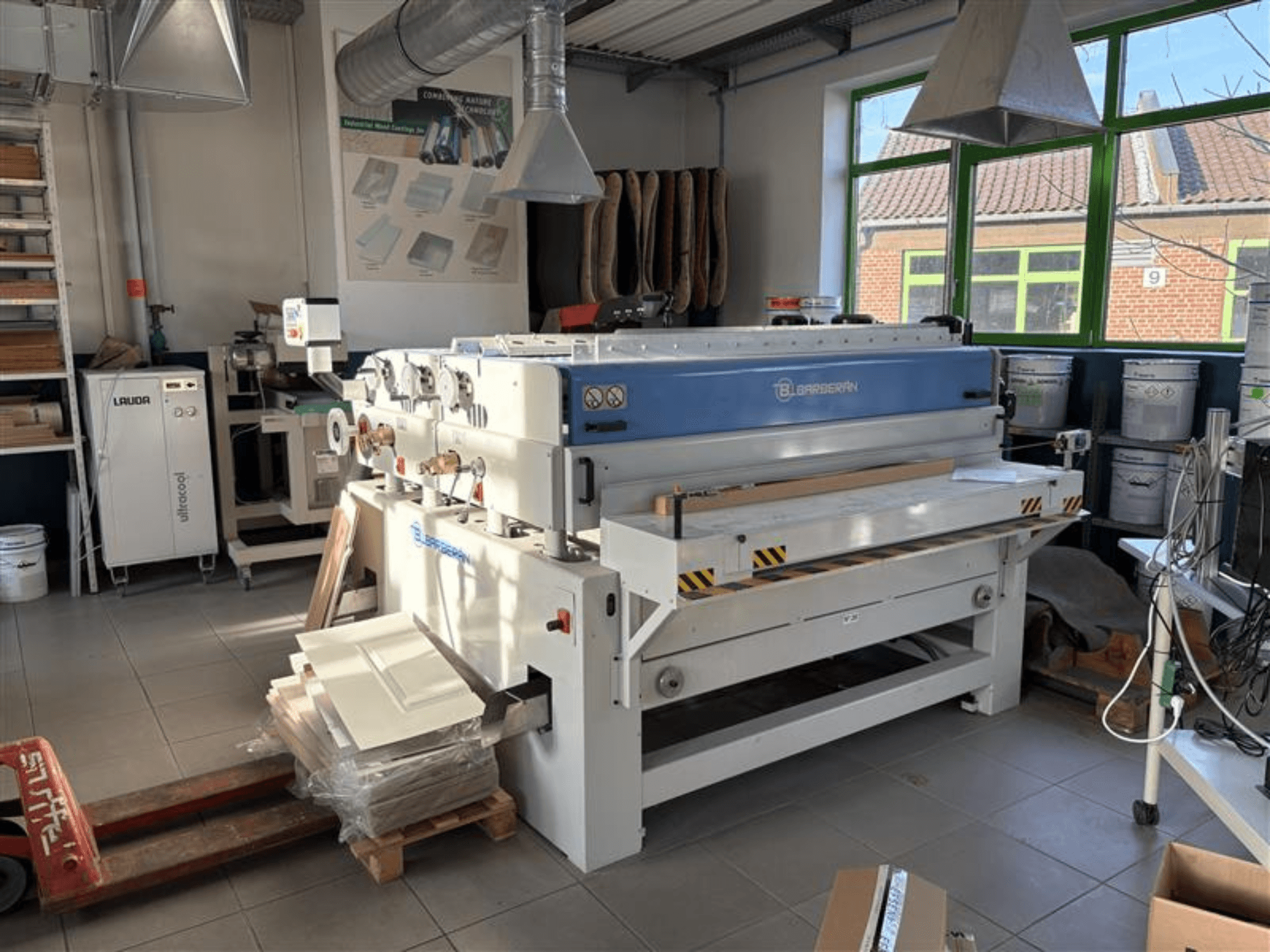 Blaserbn träbearbetningsmaskin i en verkstad, framifrån; med träpaneler på en pall och modern utrustning i bakgrunden.