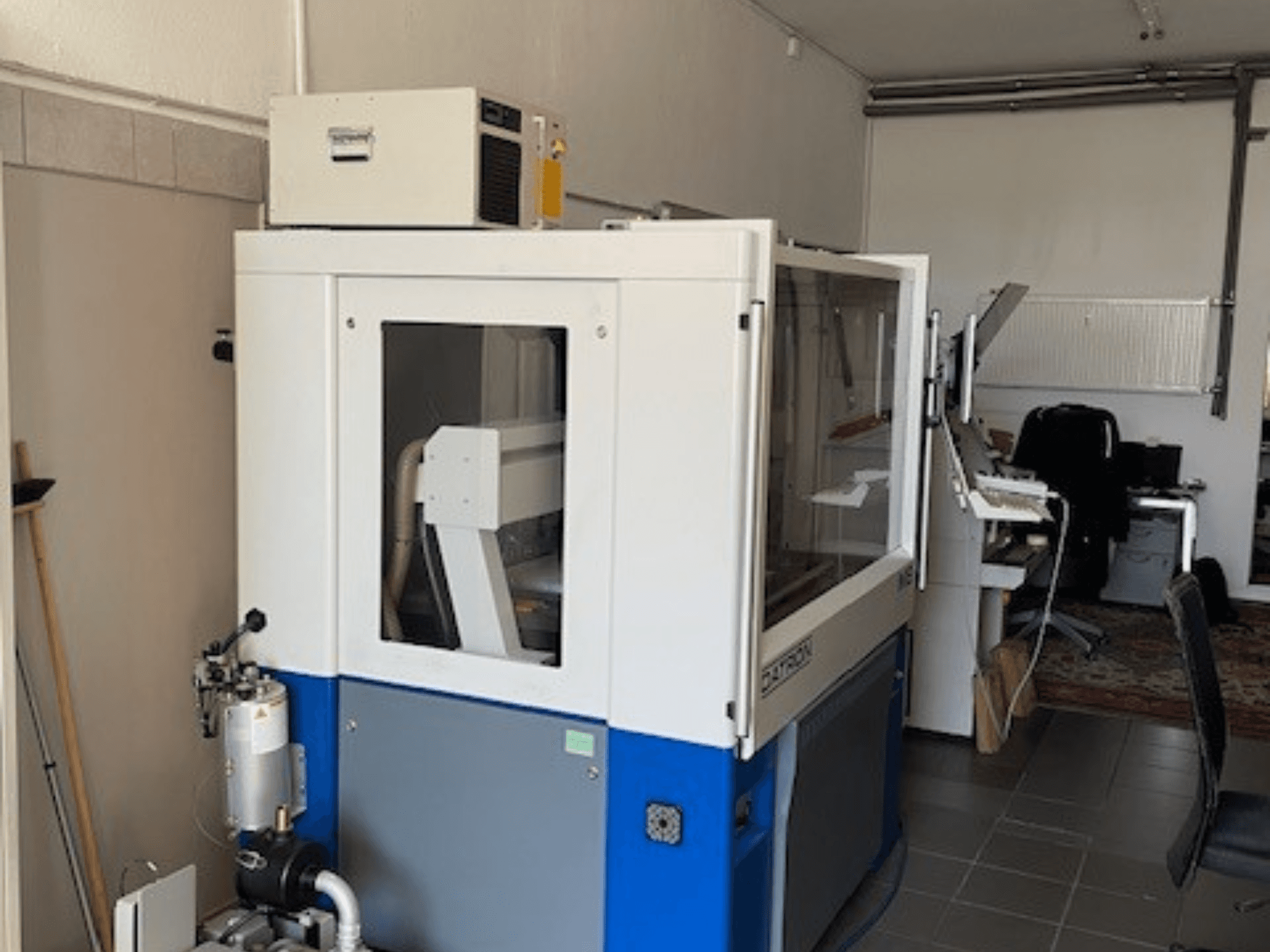 Blåvit industrimaskin med transparenta paneler, framifrån, med kontrollåtkomst och synlig ventilationsenhet.