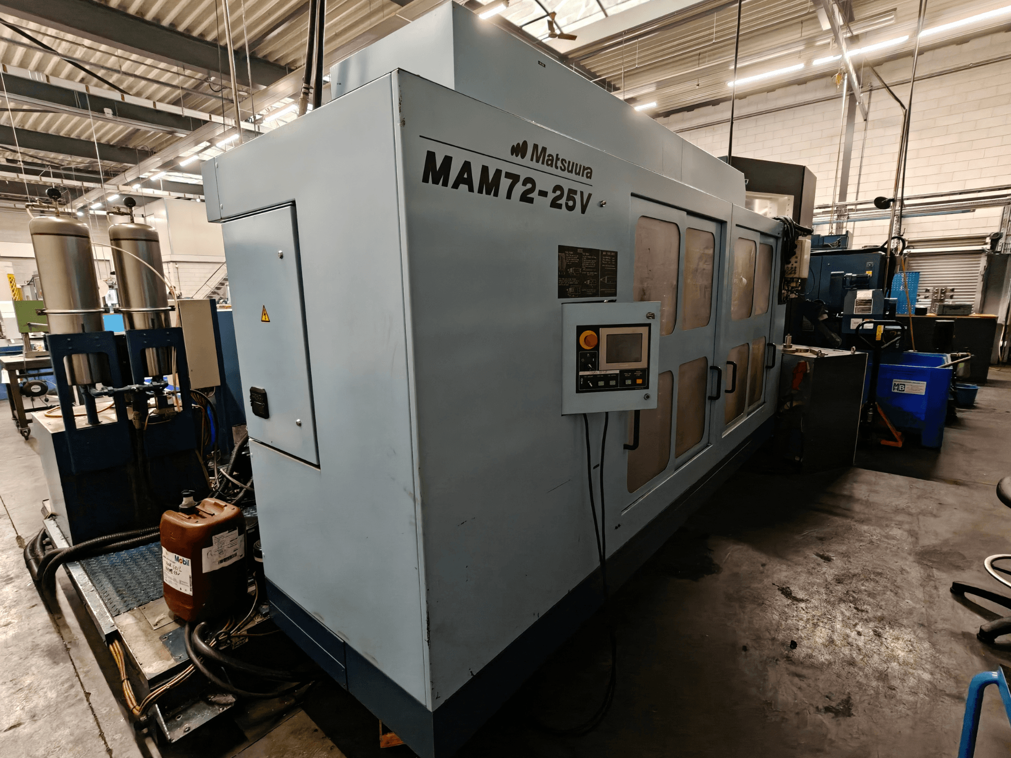 Matsuura MAM72-25V CNC-maskin, vy från sidan, med kontrollpanel, dubbla kylvätsketankar och arbetsyta i en industriell miljö.