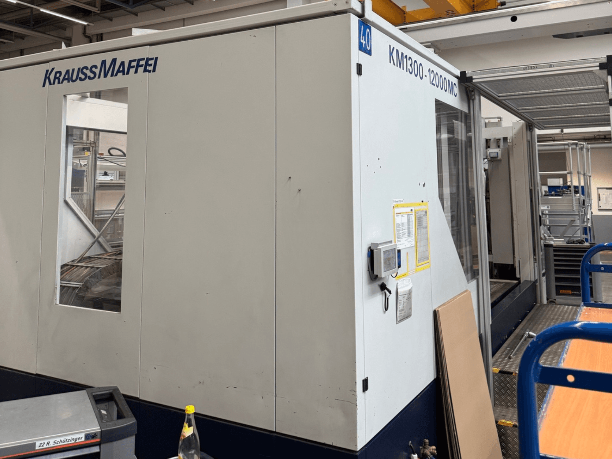 Krauss Maffei hydraulisk formsprutningsmaskin KM1300-12000 MC, sidovy som visar kontrollpanelen och driftutrymmet.