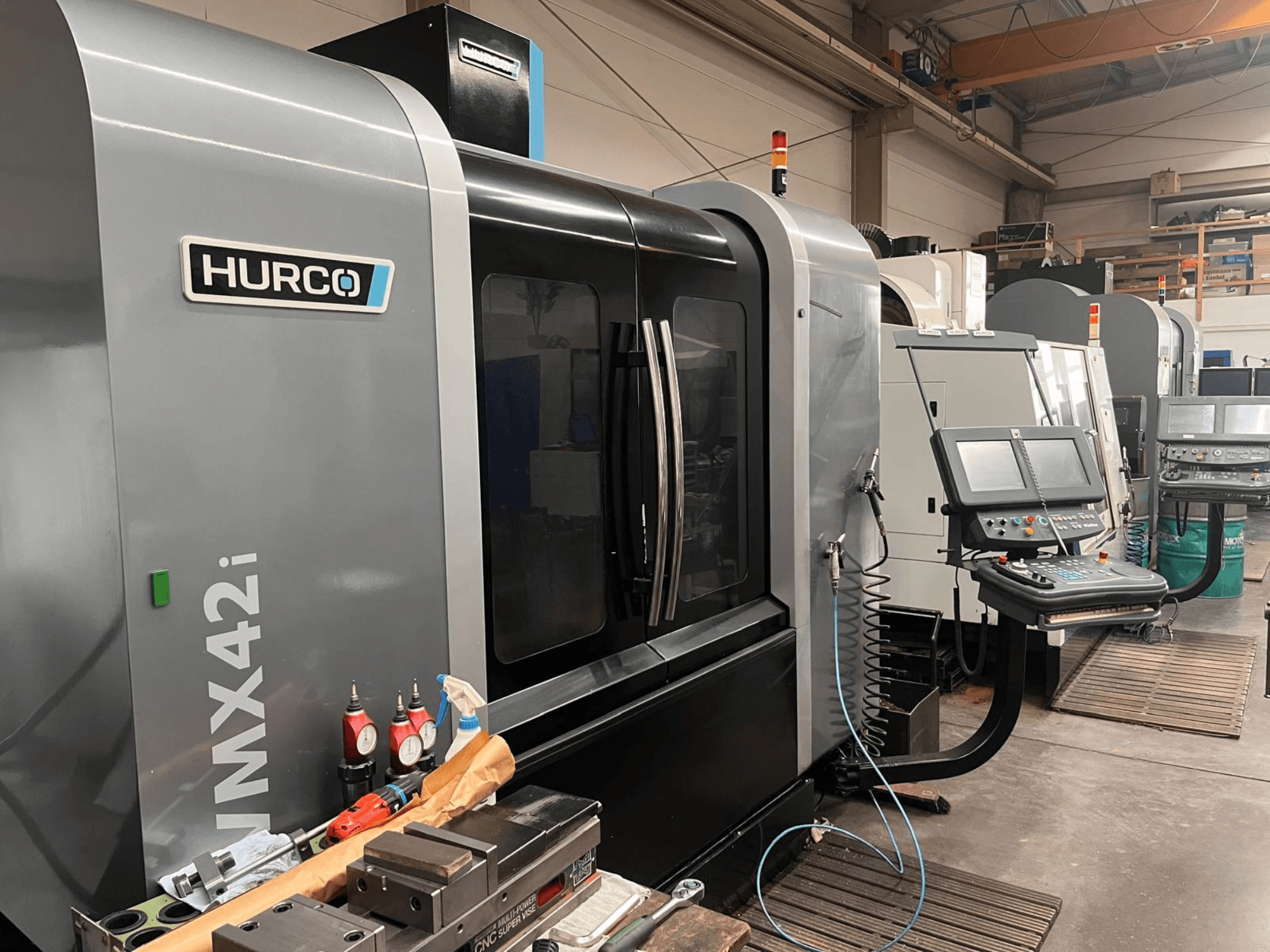 Hurco VMX42i CNC-maskin i en verkstad, vy framifrån med kontrollpanel och olika verktyg på arbetsbänken.