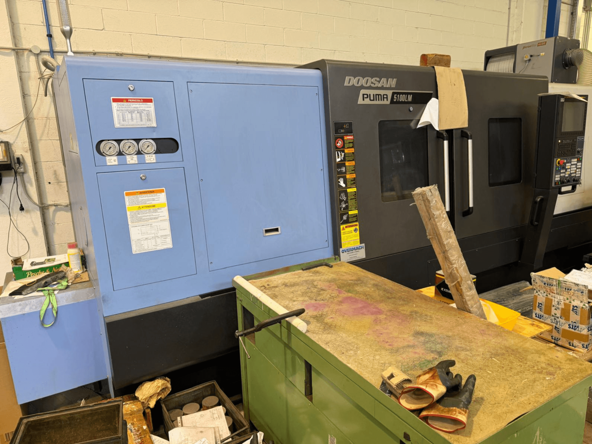 Doosan Puma 5100LM CNC-maskin och kontrollpanel, vy från sidan. Mätare och varningsetiketter synliga på den blå styrenheten.