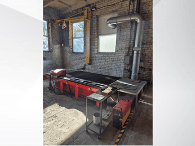 Rött CNC-plasmaskärbord med kontrollpanel och avgaskanal i metall, sett från sidan i en väl upplyst verkstad.