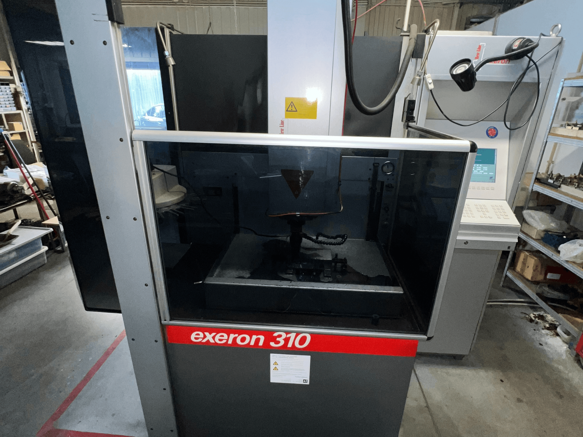 Frontvy av en Exeron 310-maskin, med en glaskammare och kontrollpanel tillsammans med arbetsstationshyllor.
