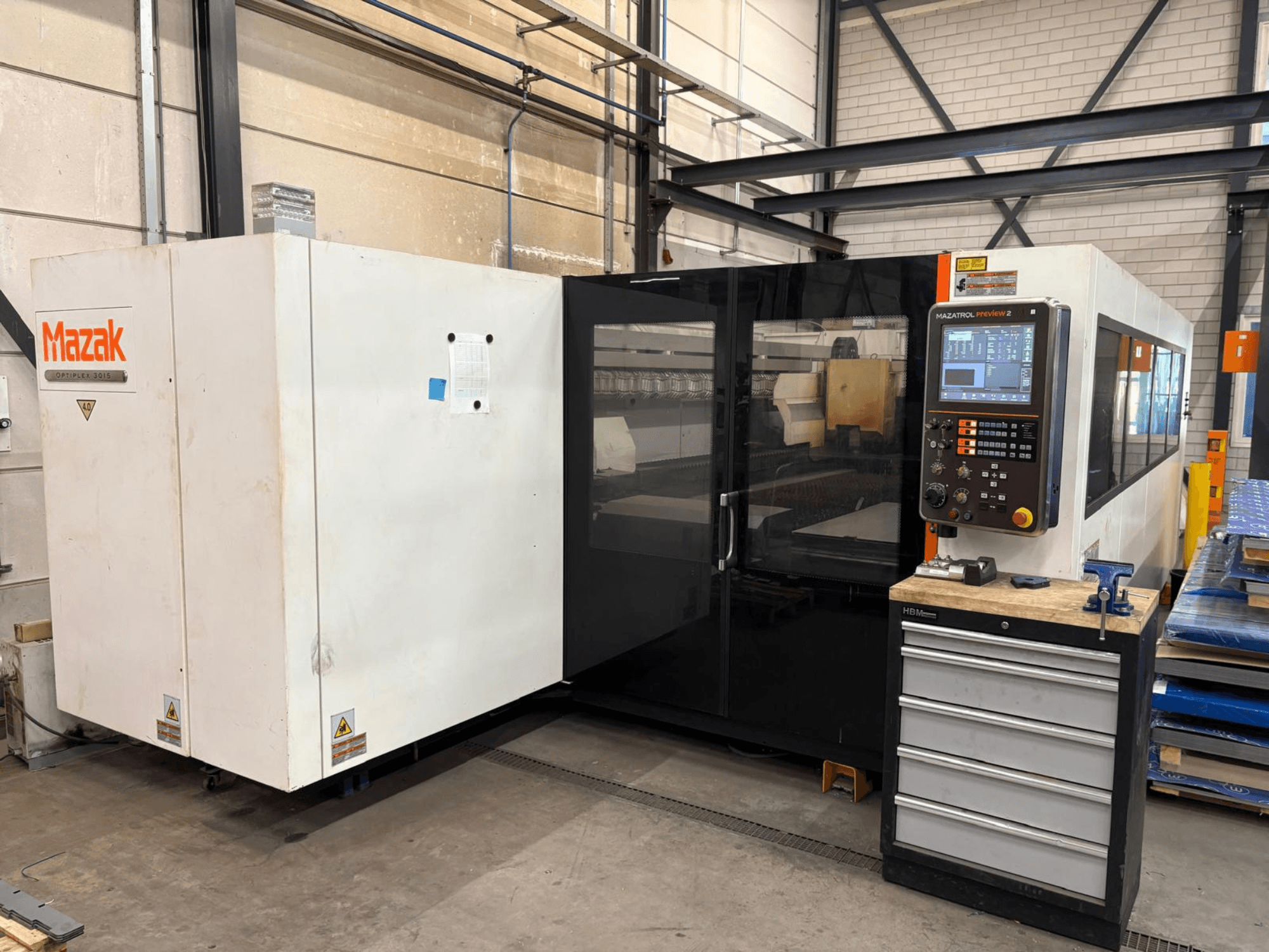 Mazak Optiplex 3015 CO₂-laserskärmaskin, framifrån, med kontrollpanelen och den industriella miljön i bild.