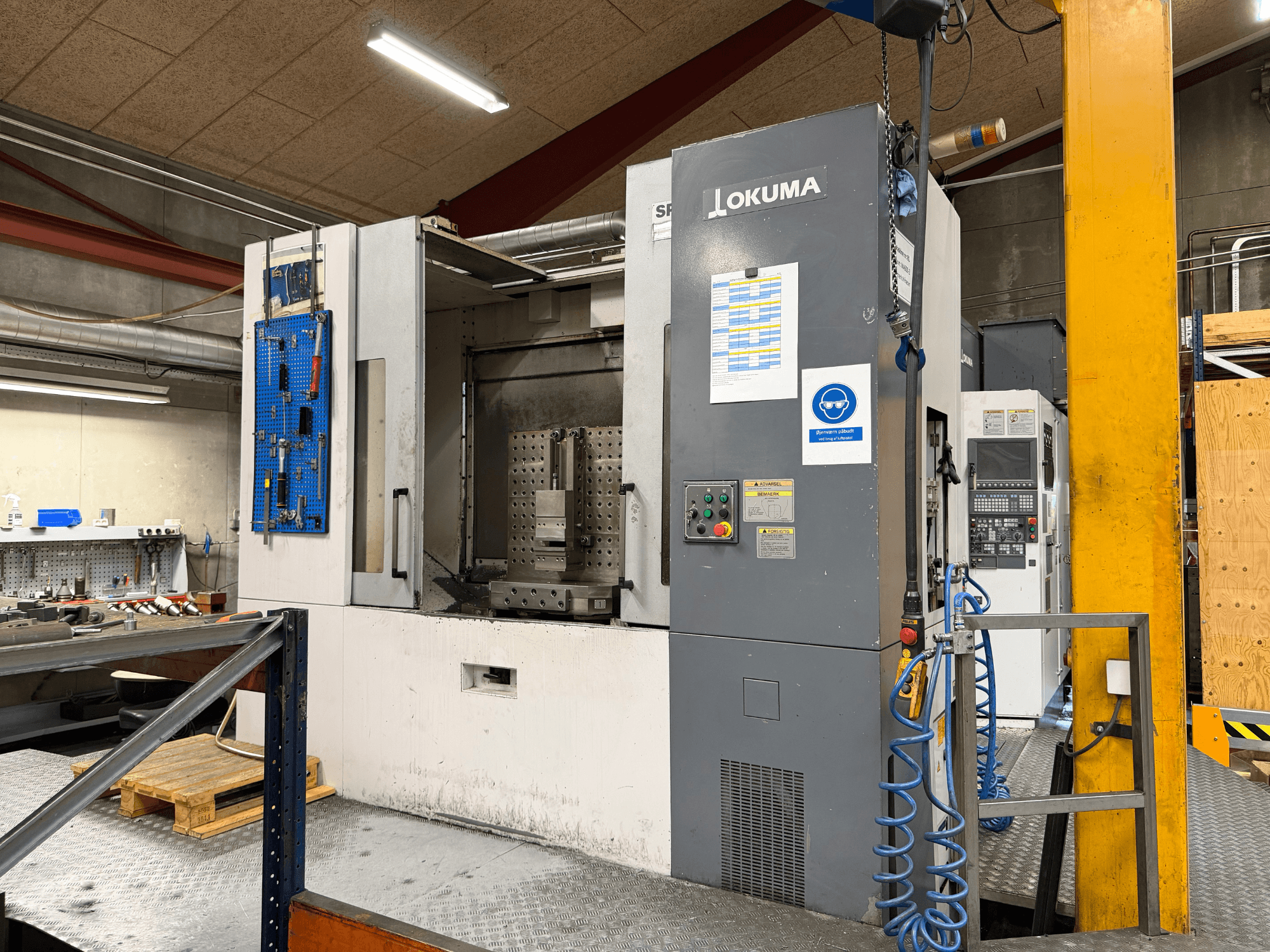 Ett horisontellt bearbetningscenter av typen Okuma MA-600HB i en verkstad, framifrån sett med kontrollpanelen och arbetsområdet.