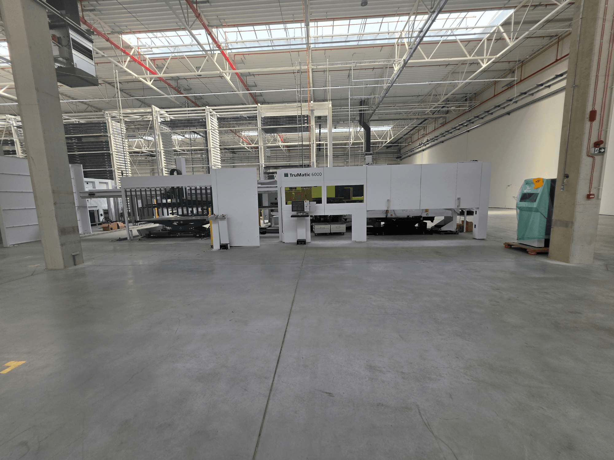 TRUMPF TruMatic 6000-1600, en kombimaskin med stans- och fiberlaser, i ett rymligt lager, sedd framifrån.