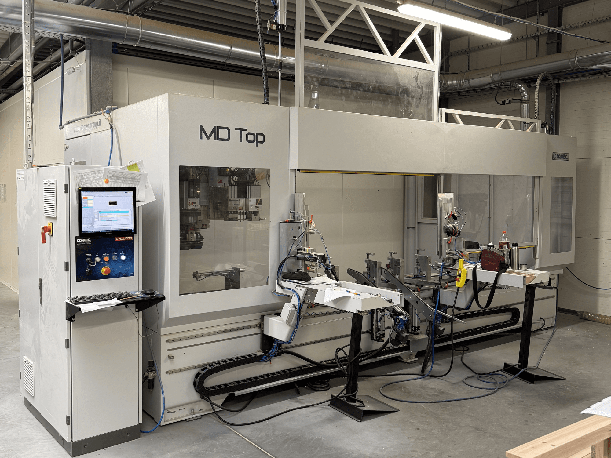 MD Top CNC-maskin sedd framifrån, med kontrollpanel, robotarmar och arbetsyta med verktyg och material.