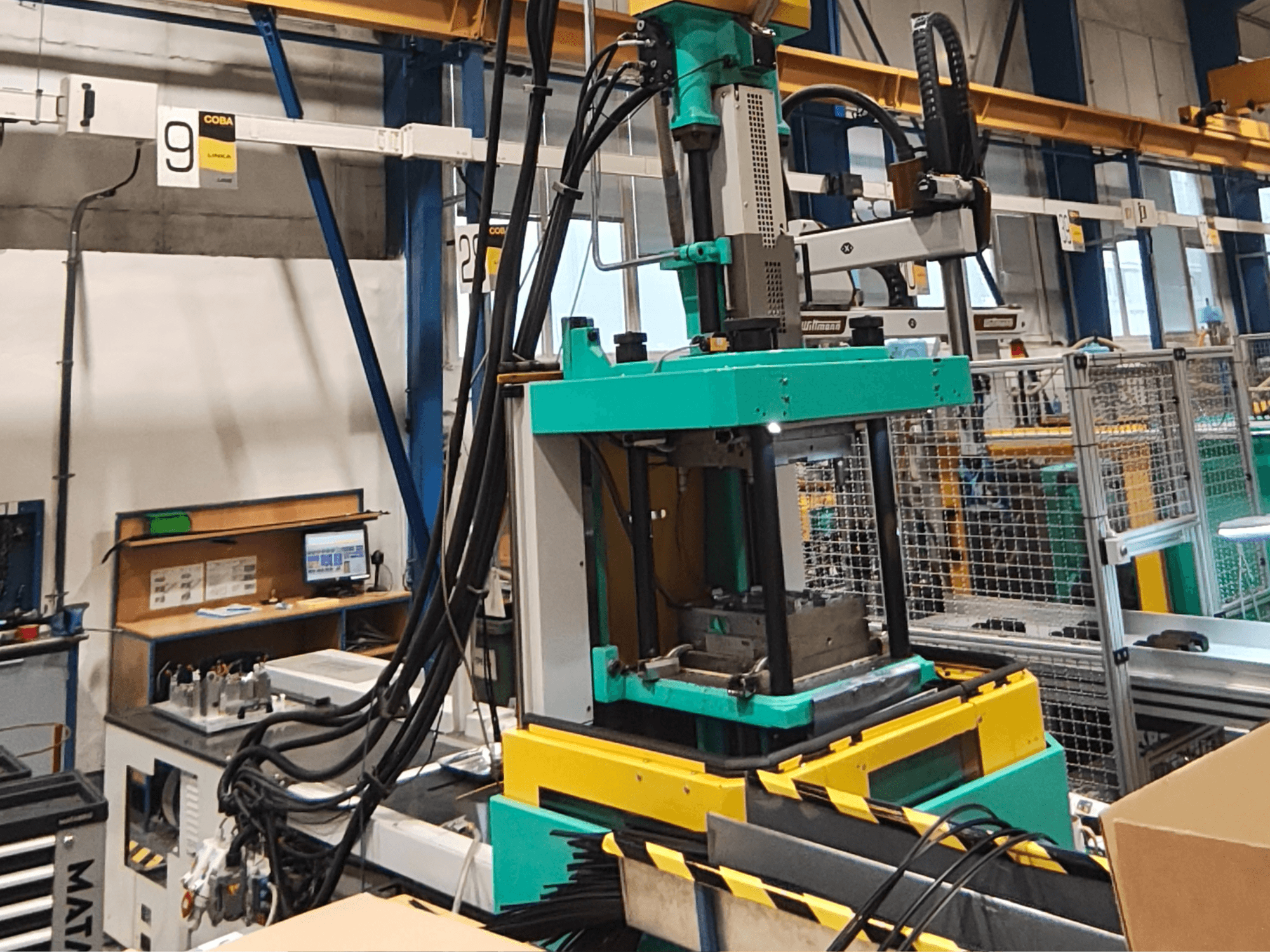 Grön och gul hydraulisk pressmaskin i en fabrik, framifrån, med synlig kontrollpanel och kablar på sidan.