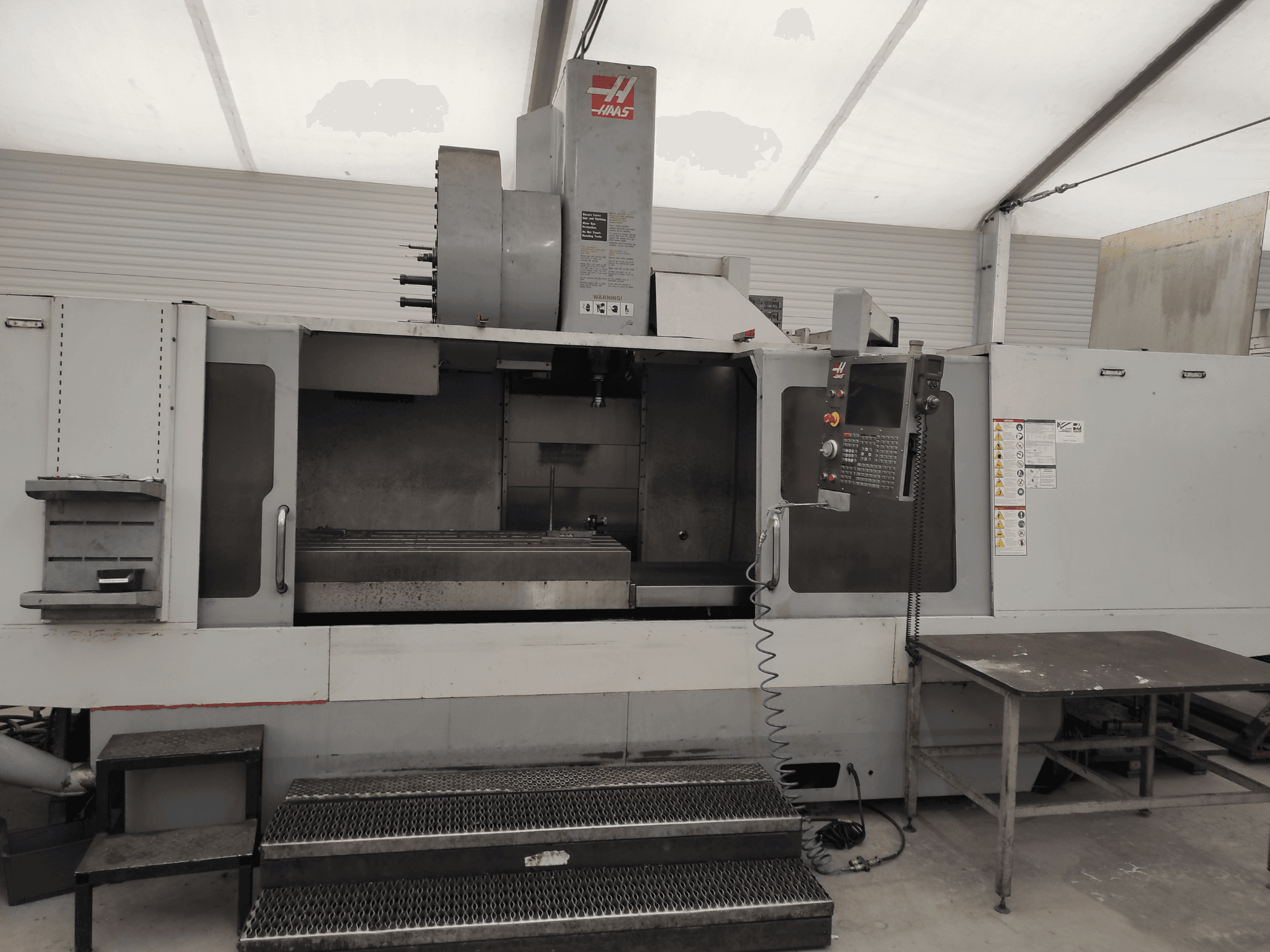 HAAS VF-10/50HE vertikal fleroperationsmaskin, framifrån med kontrollpanel, maskinbädd och åtkomligt steg för manövrering.