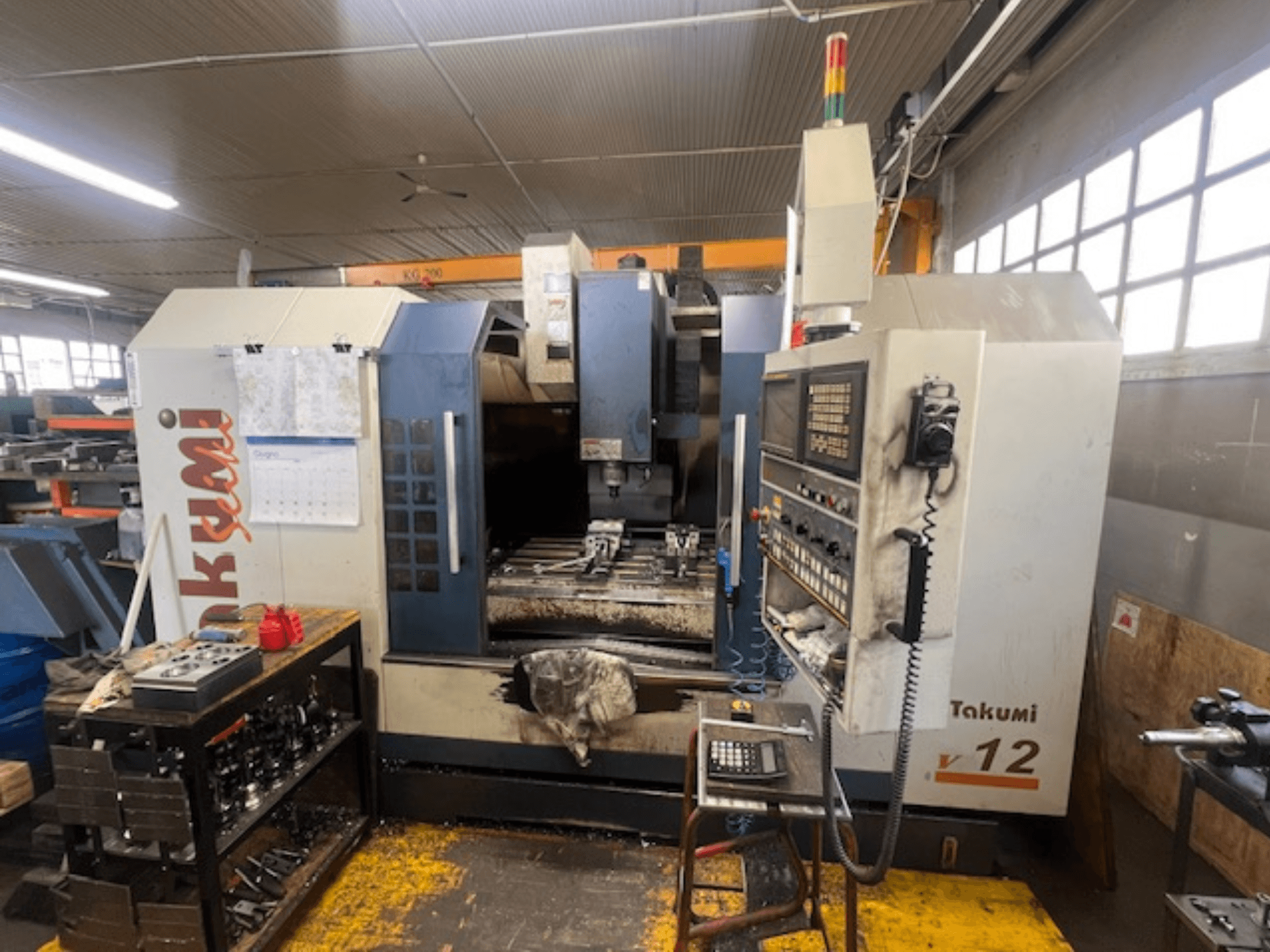 Takumi V12 CNC-fräsmaskin i sidovy, visar kontrollpanel, skärområde och verktyg på arbetsstationen.