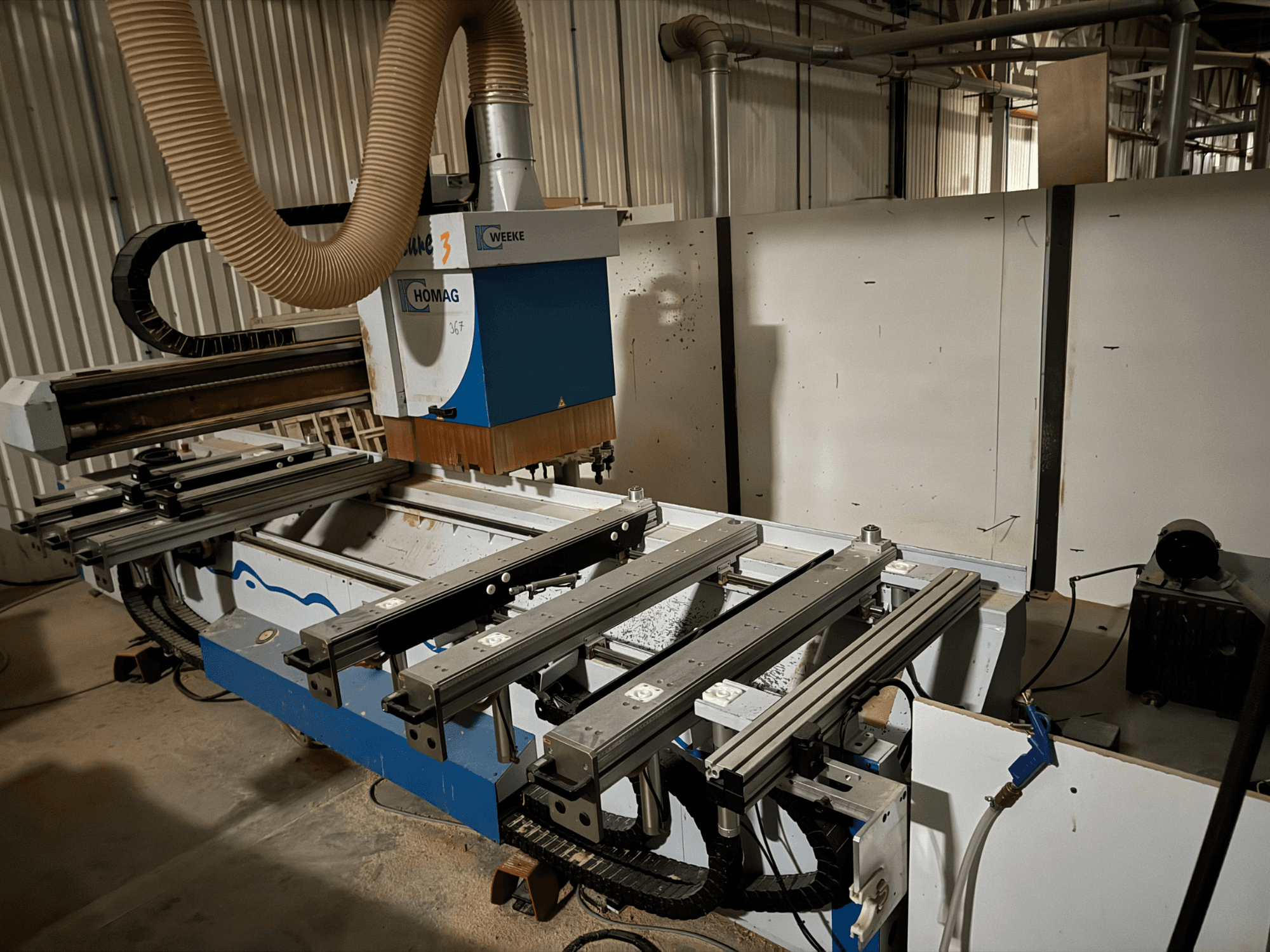 HOMAG CNC-maskin i blåvit design, vy från sidan, med glidskenor, dammutsugningssystem och monterade verktyg.