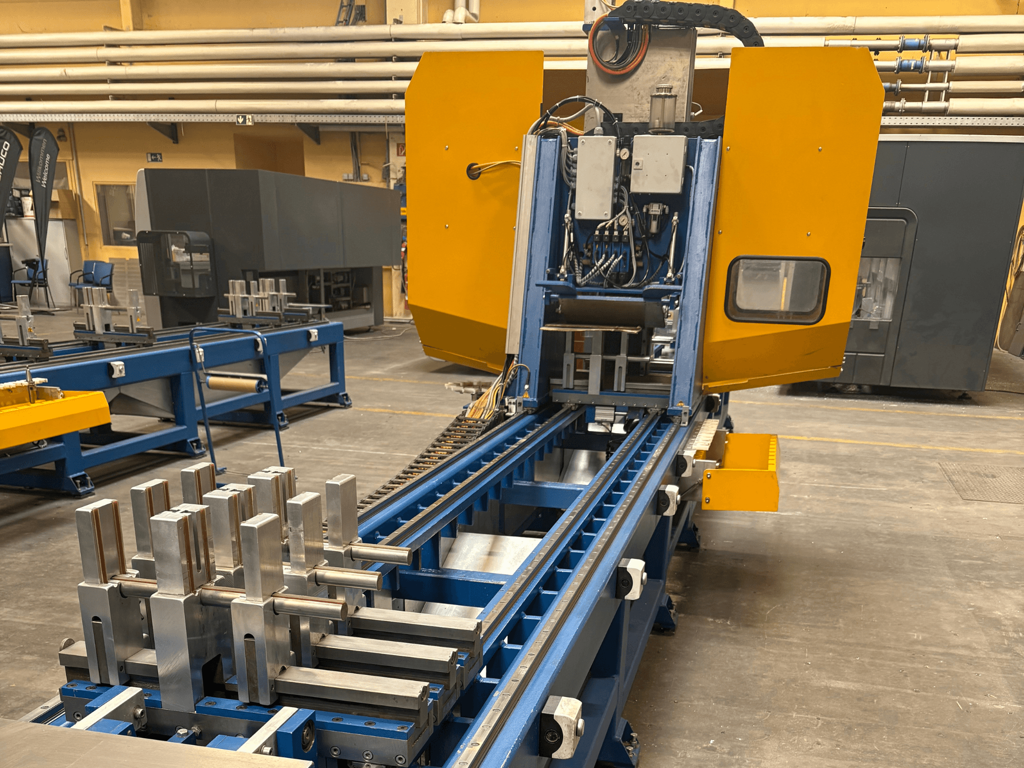 Frontvy av SCHÜCO PBX AL Universalbearbetningscenter, som visar upp metalliska arbetsstycken på en blå bearbetningsbädd.