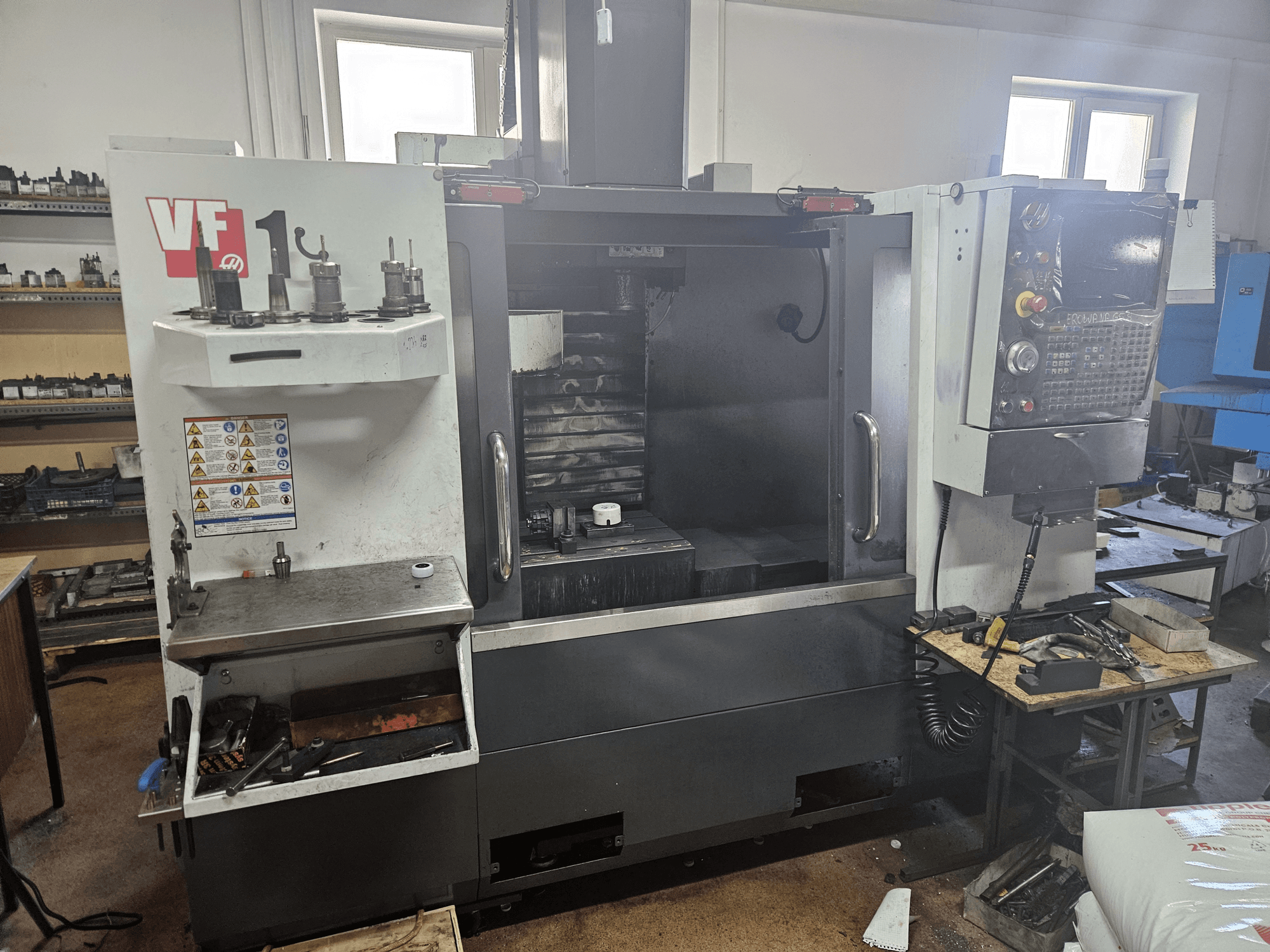 HAAS VF-1 vertikalt bearbetningscenter, framifrån med verktyg på sidan, kontrollpanelen synlig och arbetsytan i bakgrunden.