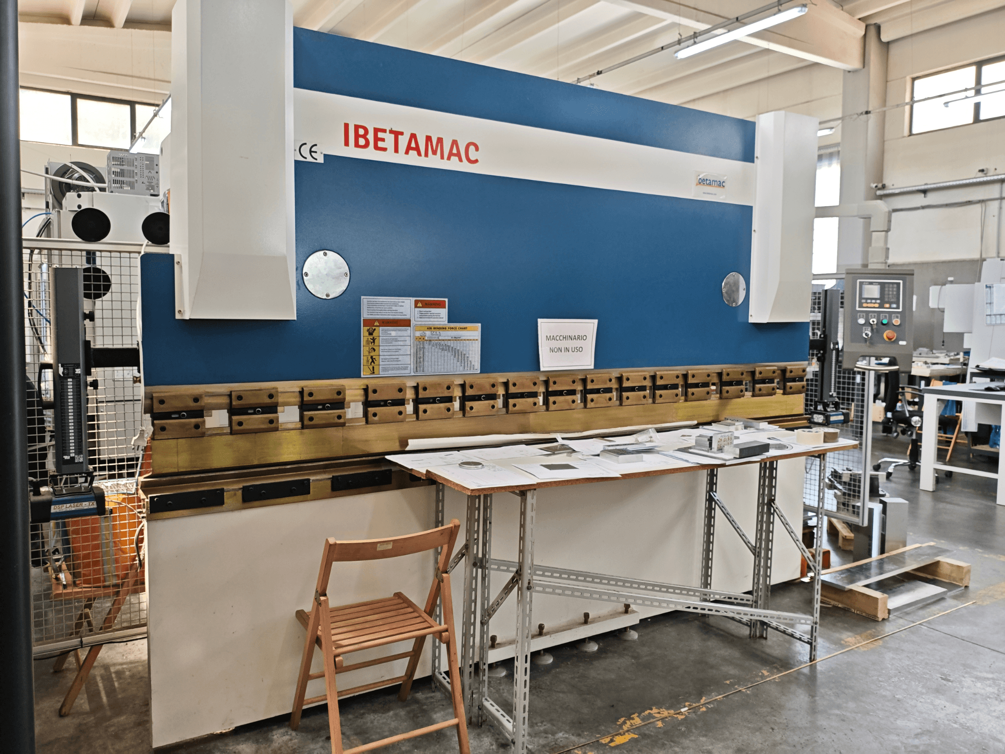 En IBETAMAC 3200 100T kantpress i en verkstad, sidovy som visar kontrollpanelen, arbetsområdet och säkerhetsanvisningarna.