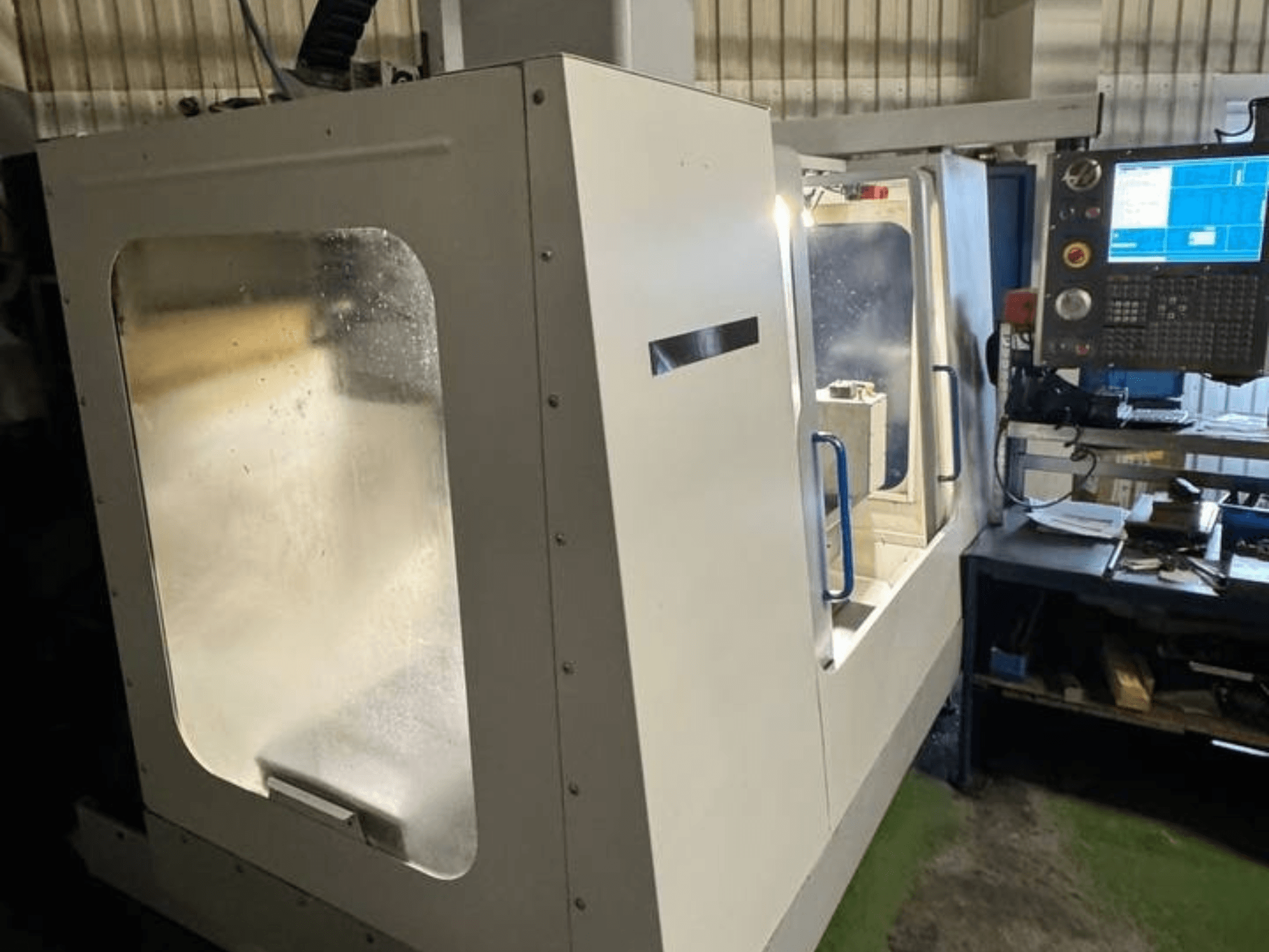 HAAS VCE 750 Vertikal fleroperationsmaskin i sidovy, med kontrollpanel och genomskinlig säkerhetshölje.