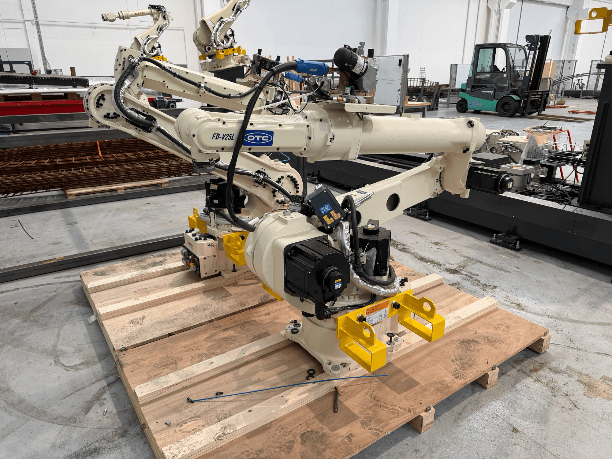 OTC Daihen FD19-V25L-robotarm sedd framifrån, med gula gripklor och synliga mekaniska komponenter på en träpall.