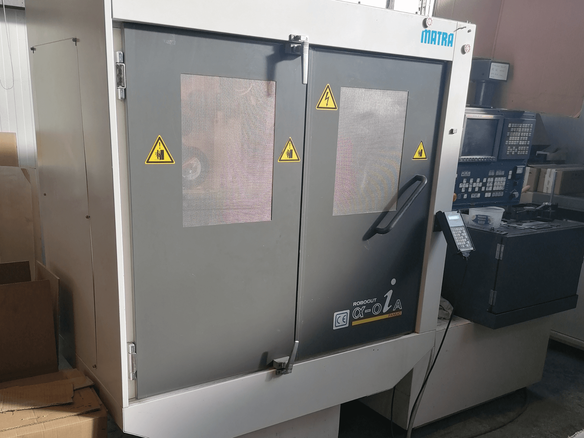 Robocut α-oZα-maskin från Matra, framifrån med säkerhetsvarningar, kontrollpanel och dubbla dörrar med nätfönster.