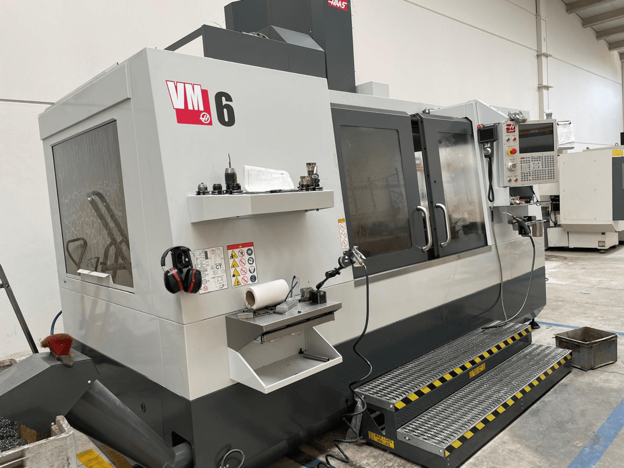 Haas VM-6 vertikala fleroperationsmaskin, frontvy med kontrollpanel, verktygshållare och säkerhetsfunktioner.