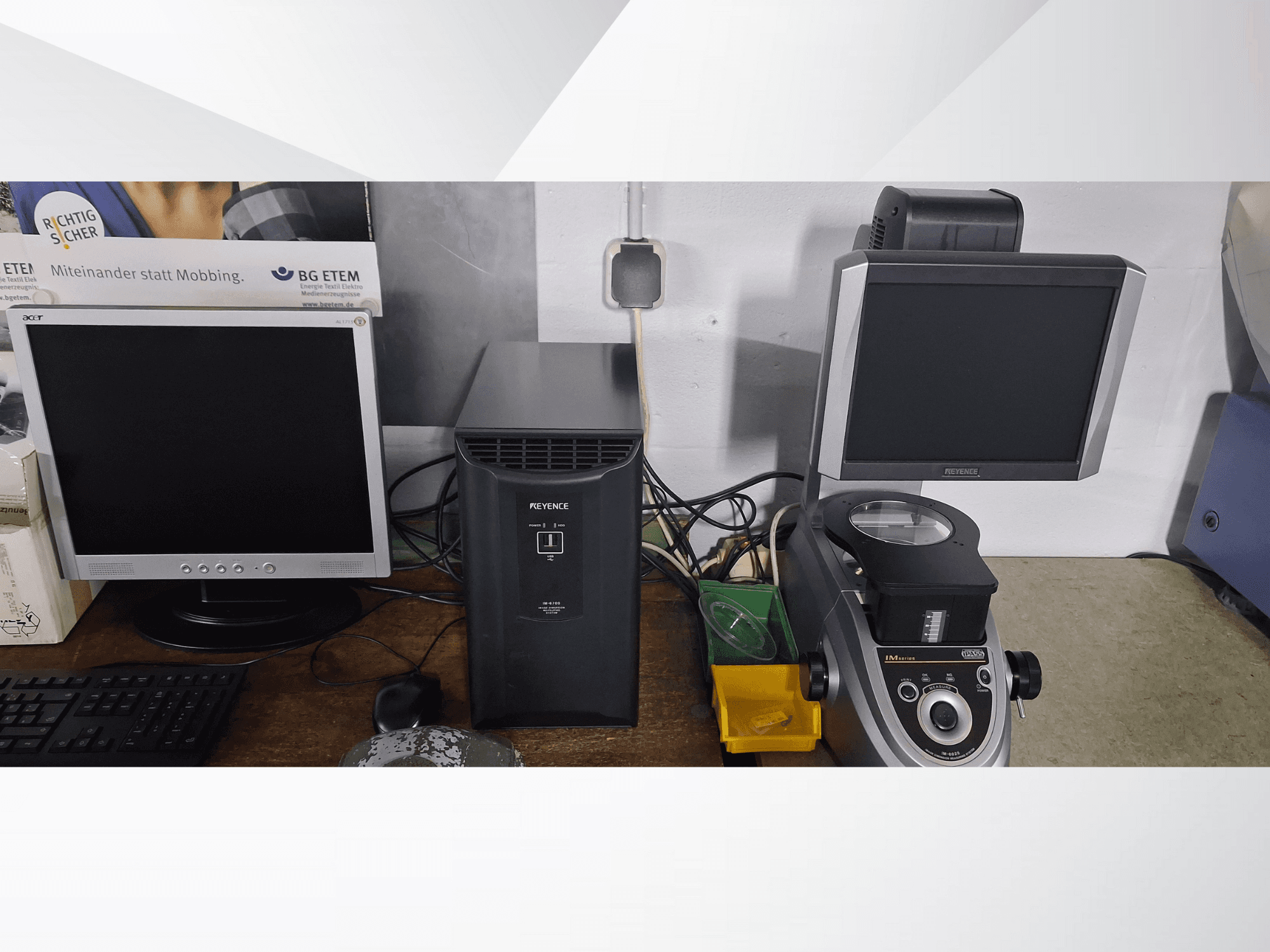 Två datorskärmar, en Acer och en Keyence, bredvid en svart apparat och ett mikroskop, sett framifrån.