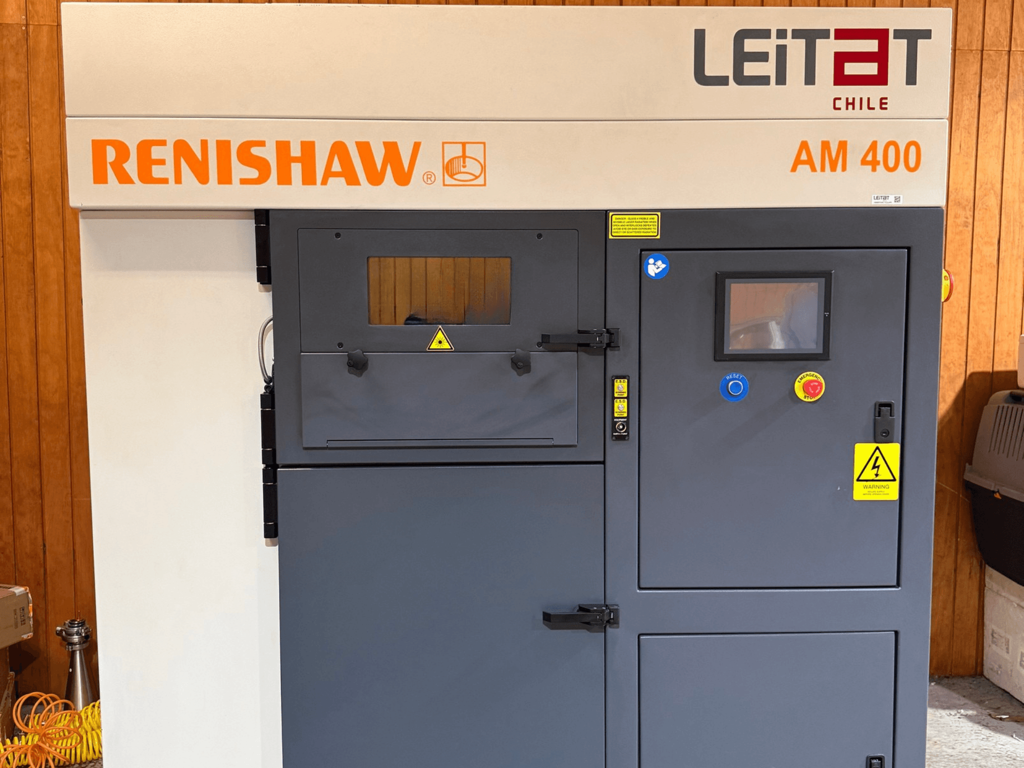 Framifrån sett på RENISHAW AM400 3D-skrivare för metall, med kontrollpanel, varningsetiketter och åtkomst för underhåll.