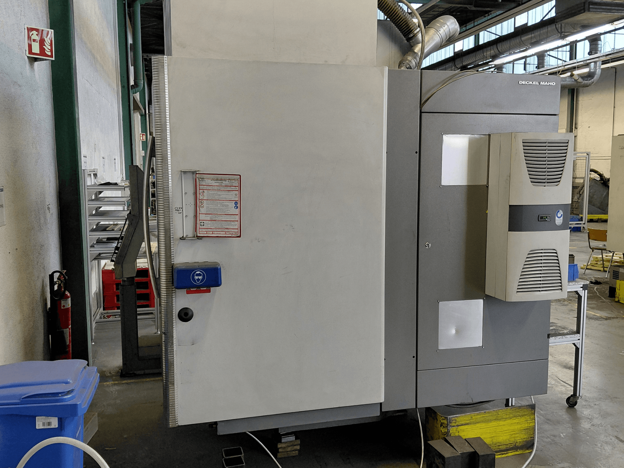 Sidovy av DECKEL MAHO DMC 635 V vertikal bearbetningscenter med kontrollpanel och säkerhetsetiketter synliga.