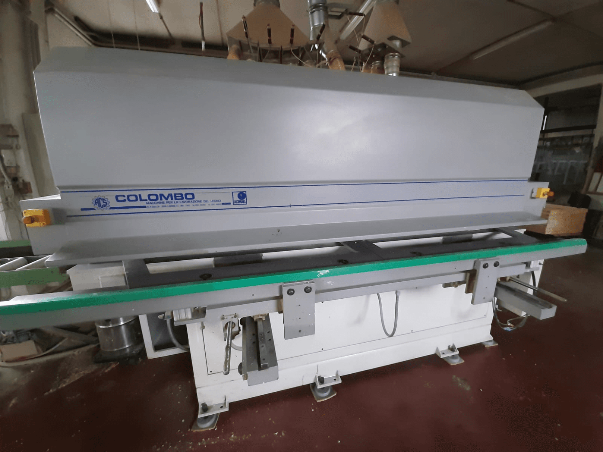 Träbearbetningsmaskin av märket Colombo, framifrån, med ett långt grönt bord, kontrollknappar och en grå kropp med blå accenter.
