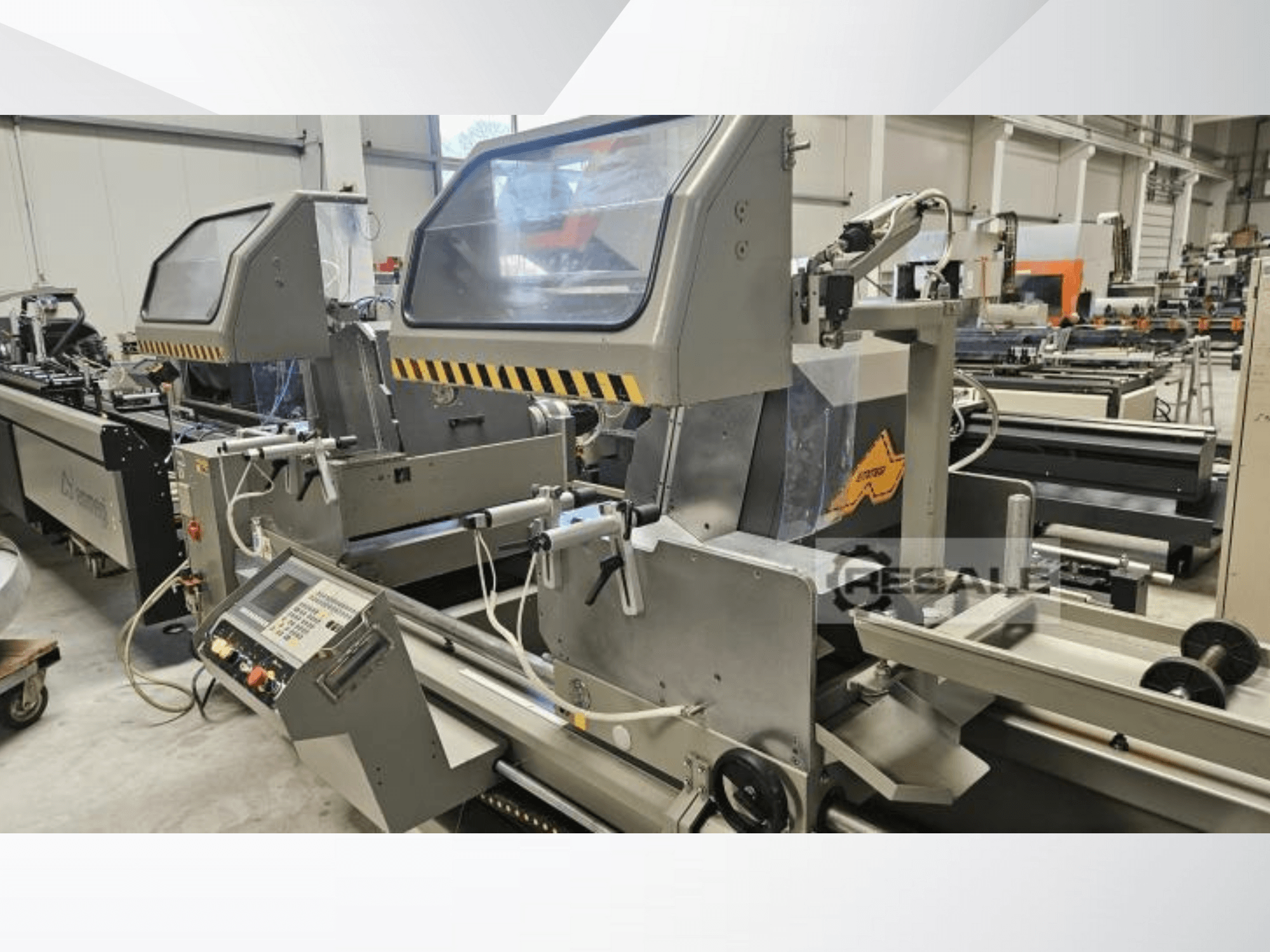 Dubbelsågsmaskiner i fabriksmiljö; framifrån med kontrollpanel, glasluckor och skärande komponenter.