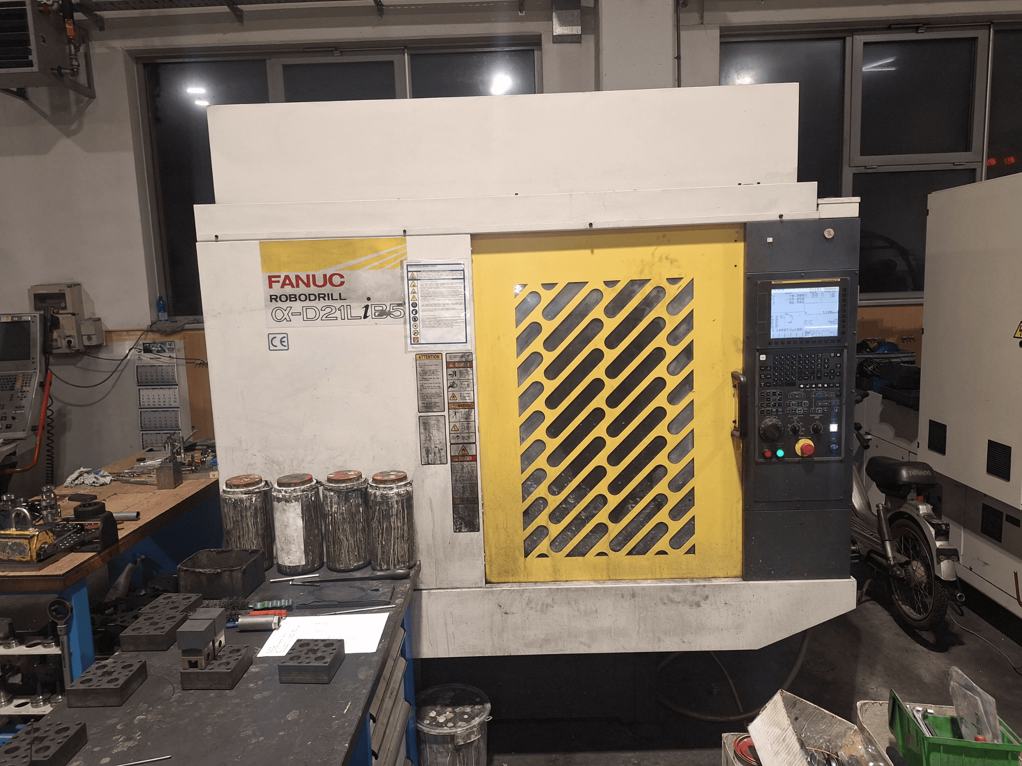 Frontvy av FANUC Robodrill α-D21LiB5, som visar kontrollpanelen, det gula gallret och närliggande verktyg på en arbetsbänk.
