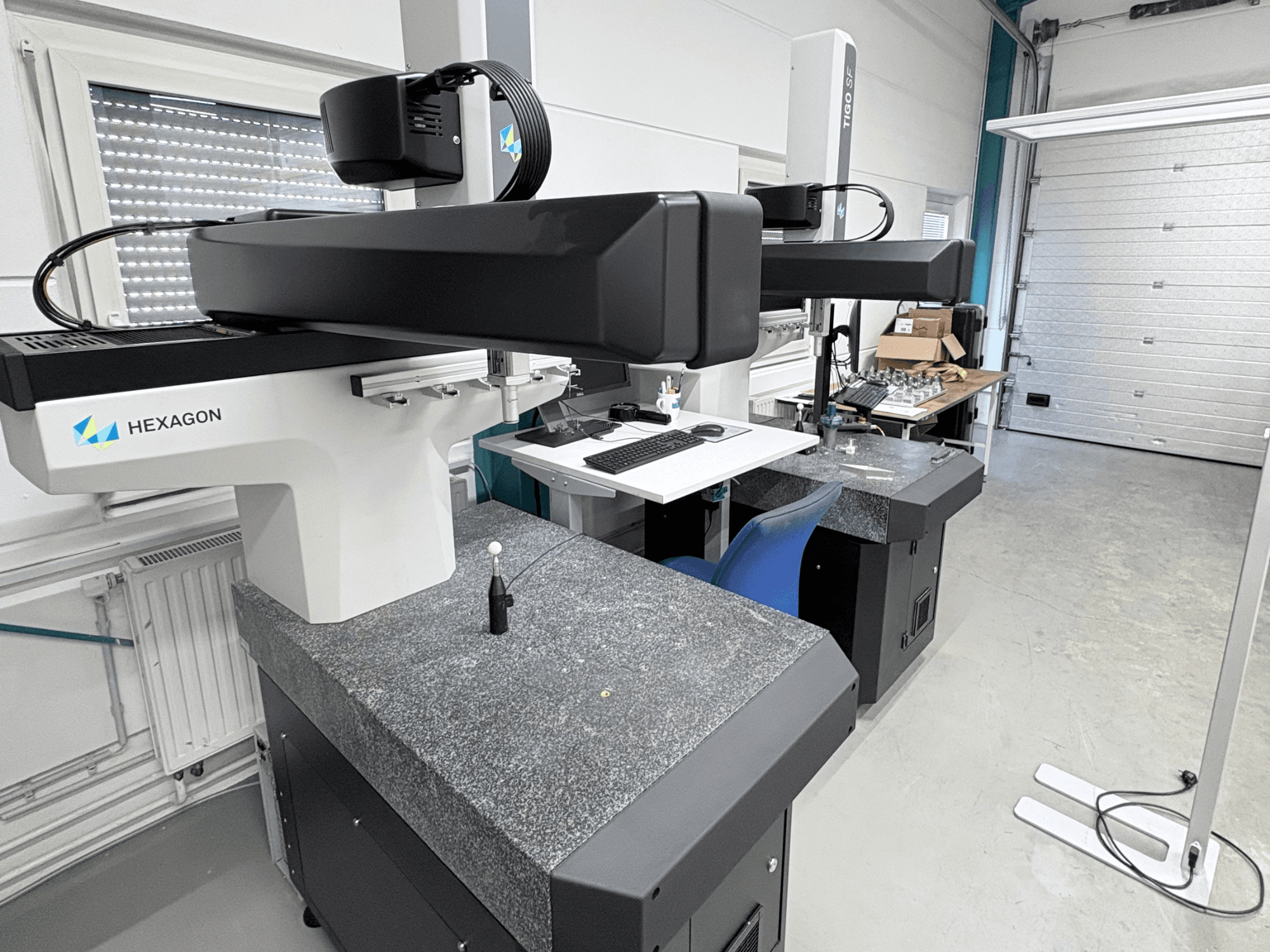 Hexagon Tigo SF CMM i verkstaden, med granitbas, mätprob och en närliggande arbetsstation med verktyg.