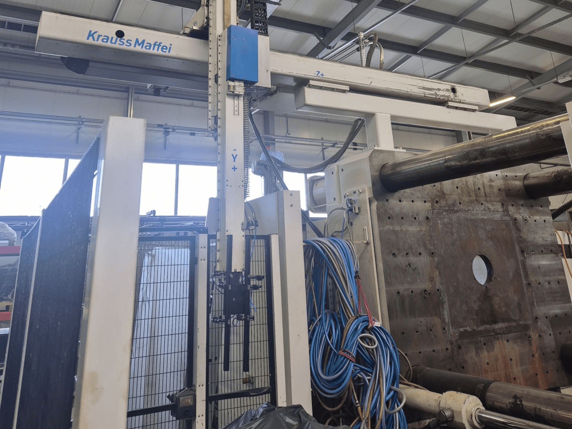Krauss Maffei 1300-12000 MX hydraulisk formsprutningsmaskin, framifrån sett med mekaniska armar och hydrauliska anslutningar.