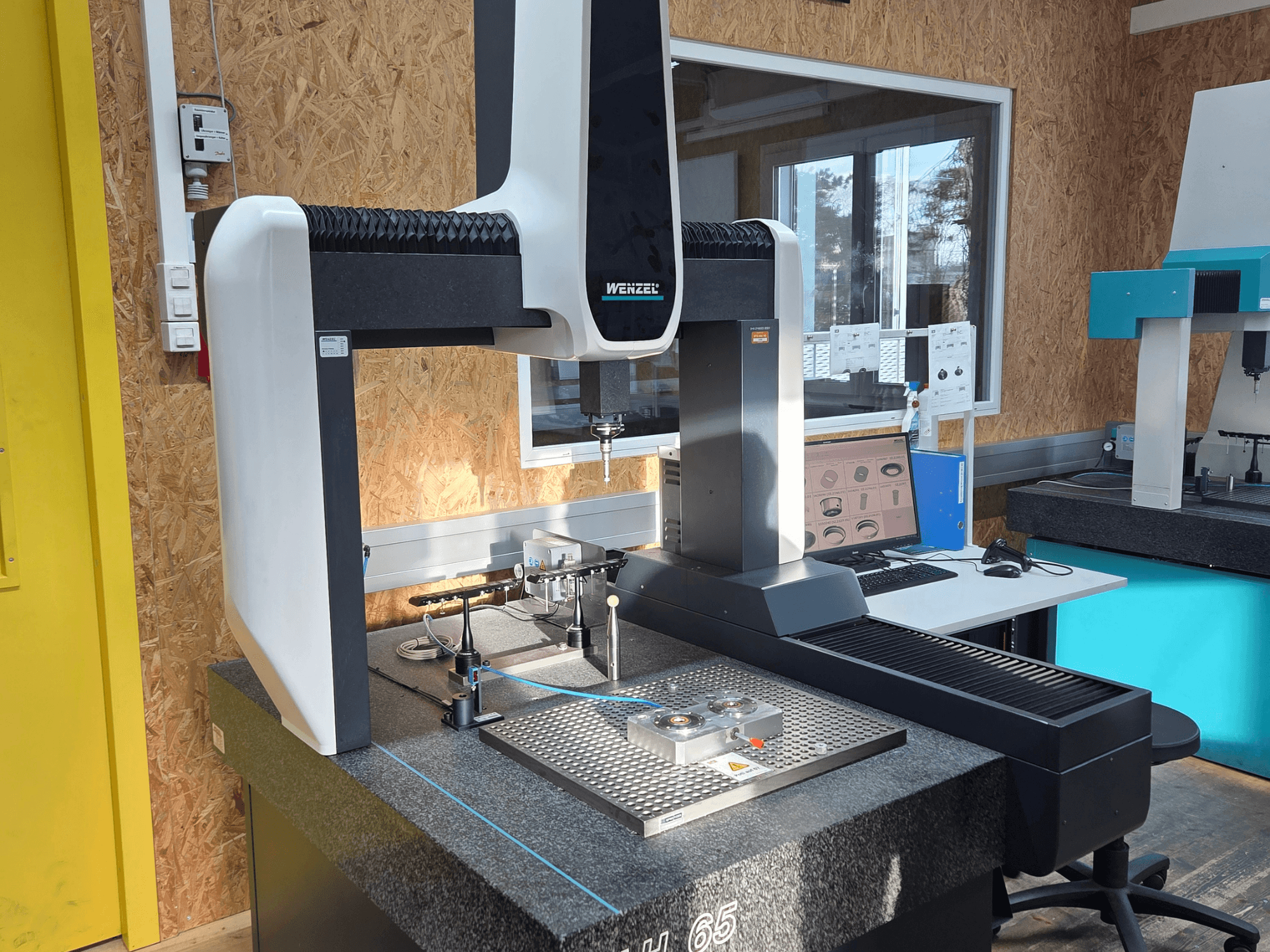 Wenzel LH 65 koordinatmätmaskin i en labbuppställning, vy framifrån, med mätverktyg och en monitor.