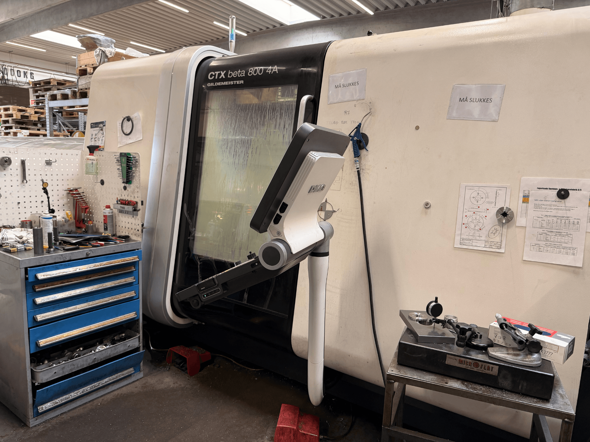 DMG MORI CTX Beta 800 4a vertikal svarv i en verkstad, med en styrarm och tekniska dokument i närheten.
