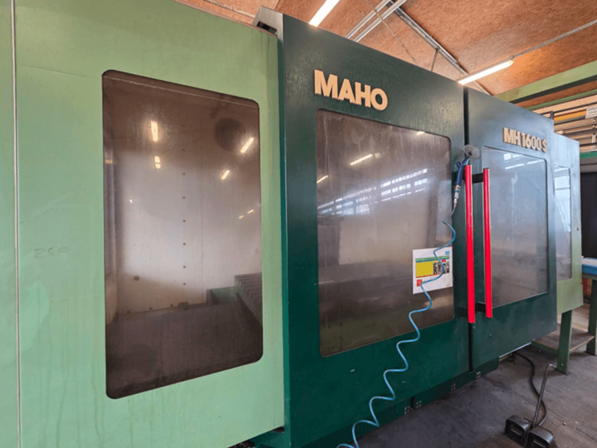 Frontvy av MAHO 1600S Universal Machining Centre, med dubbla transparenta paneler och kontrollpanel med röda handtag.