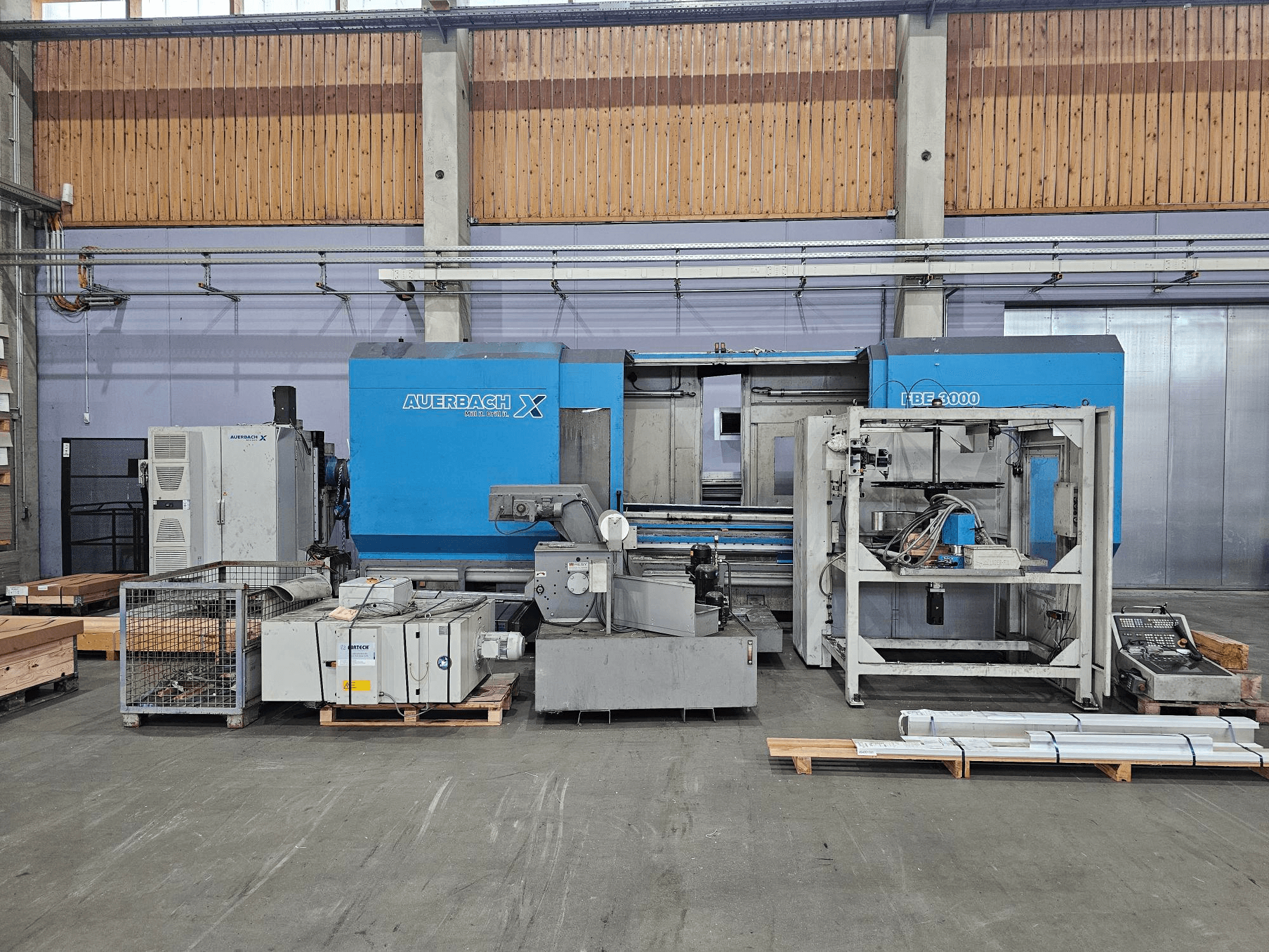 Auerbach X LBF-3000-maskin i fabriksmiljö, vy från sidan, med grå och blå komponenter och synlig kontrollpanel.