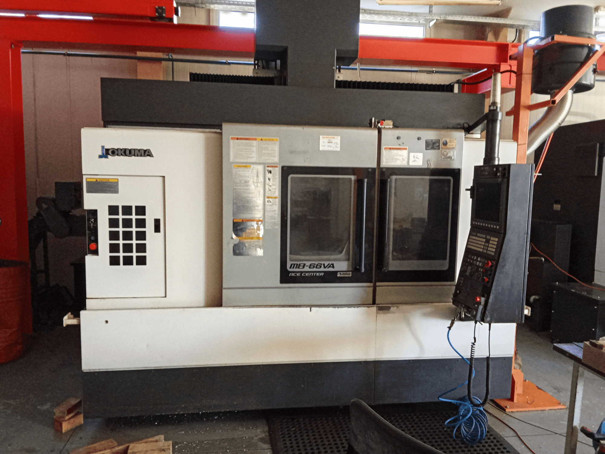 Okuma MB-66VA vertikal fleroperationsmaskin, framifrån med kontrollpanel och dubbla fönster för åtkomst av verktyg.